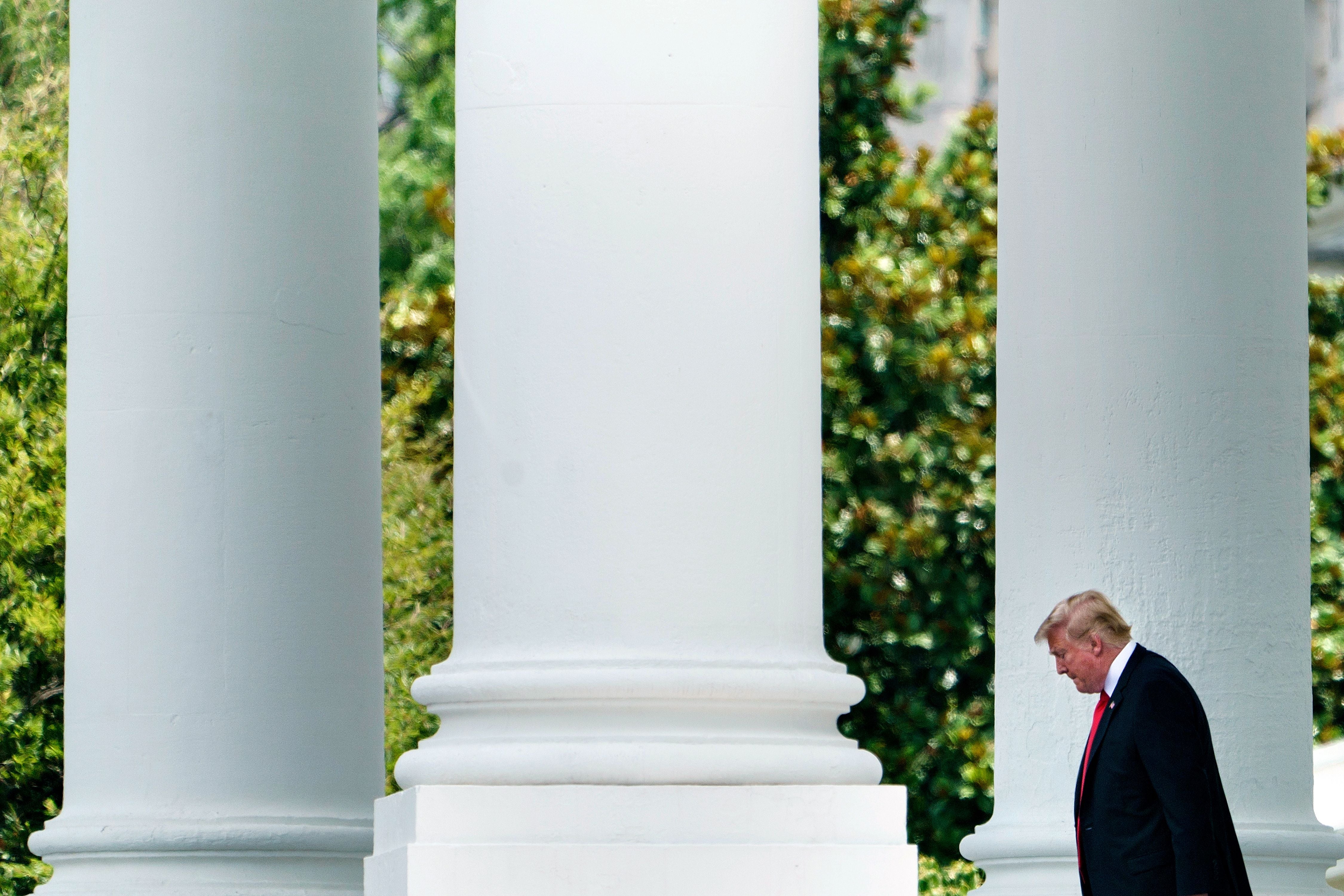 Donald Trump walks by three massive white columns.