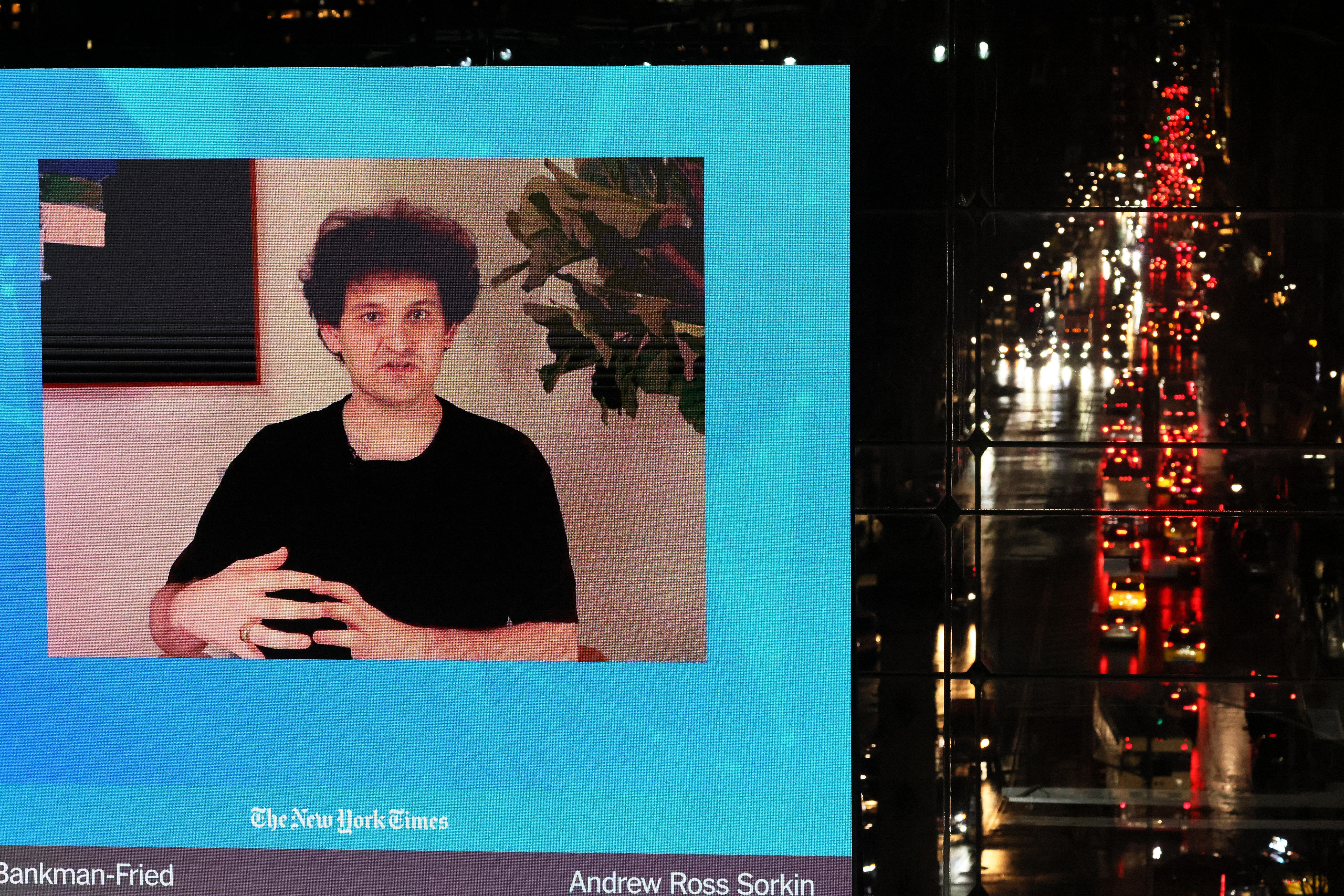 Sam Bankman-Fried speaks on a giant screen located above a car- and rain-soaked street.