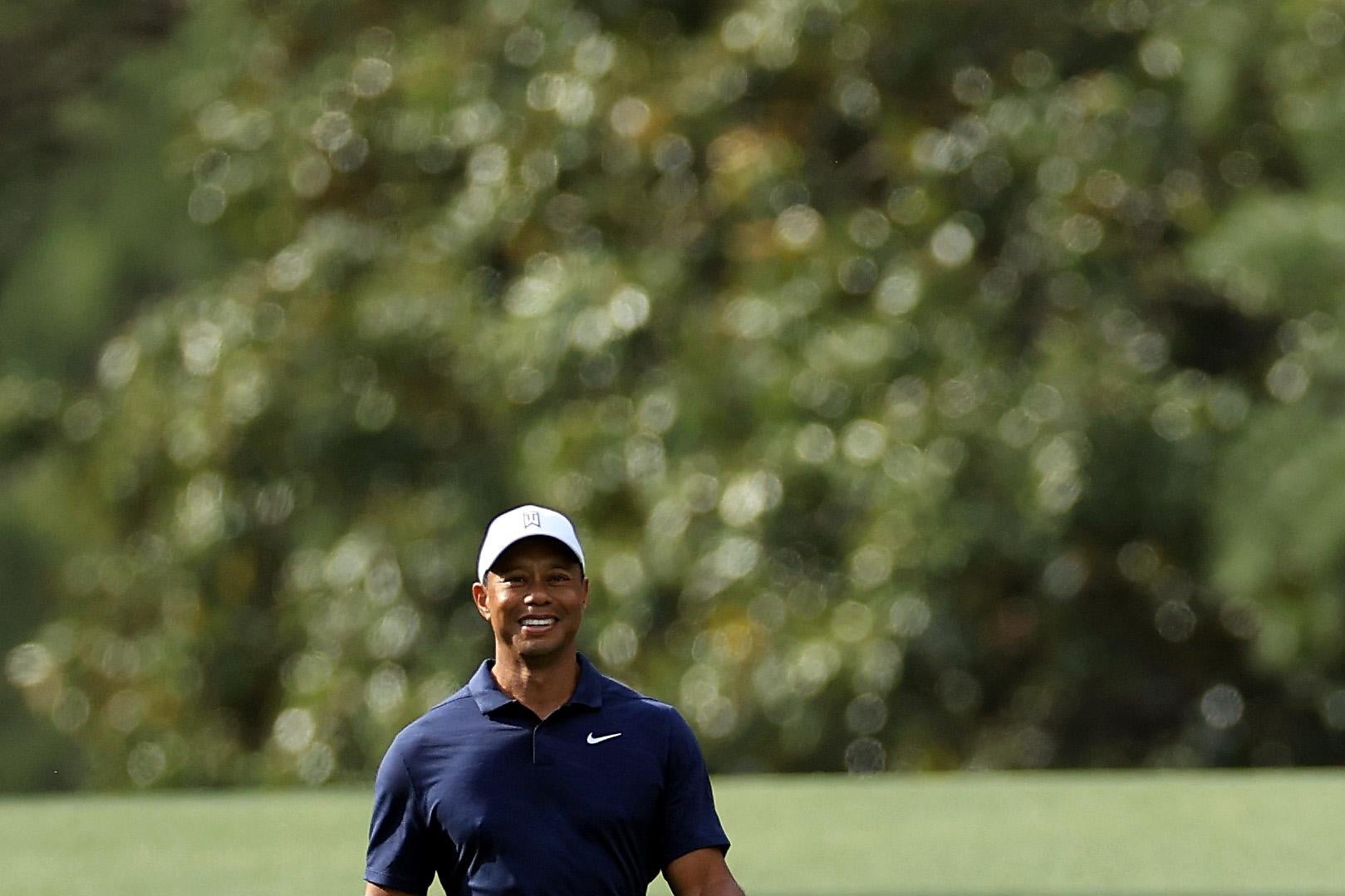 Woods walking and smiling, club in his right hand