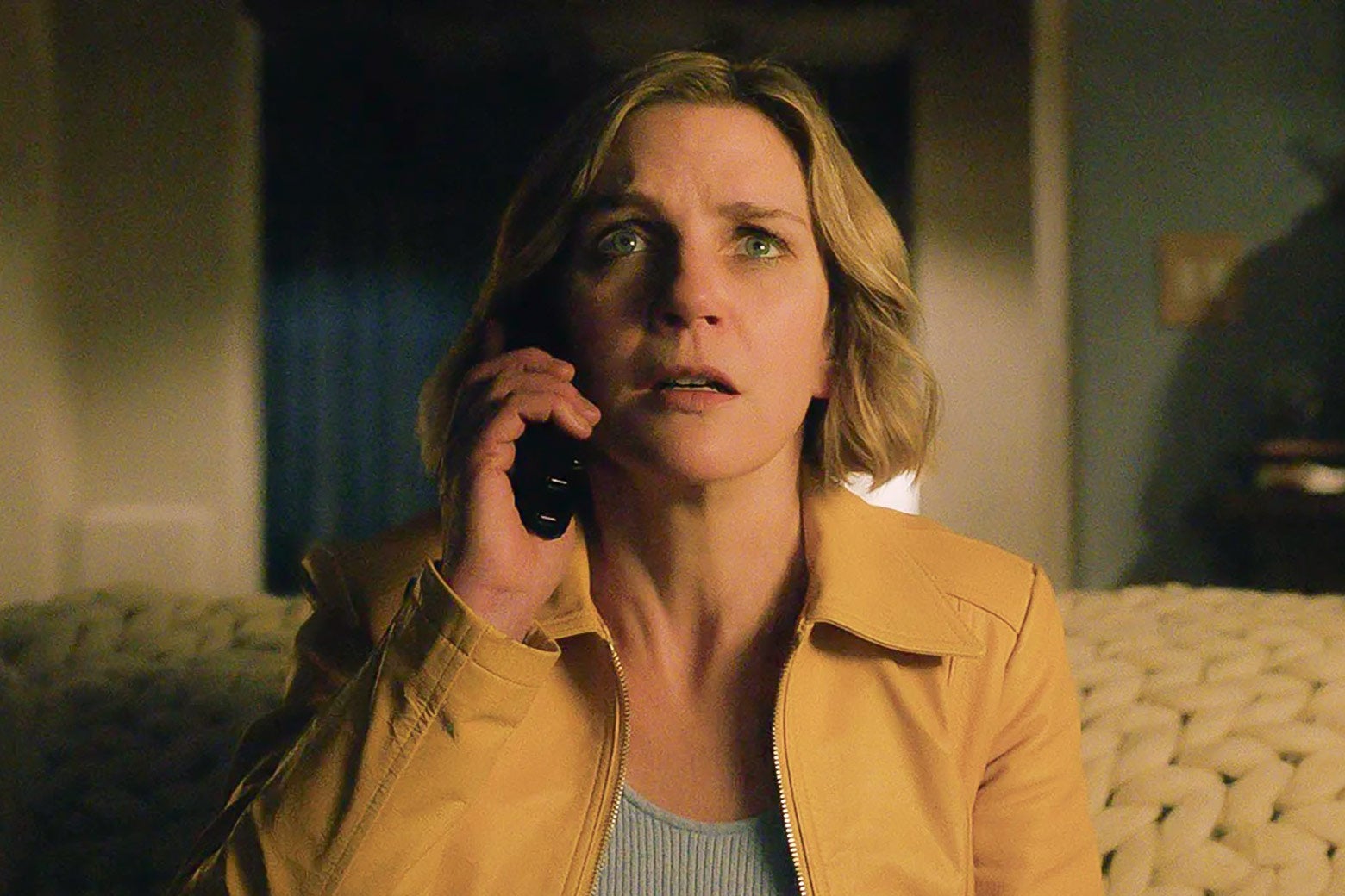 A blond woman holds up a phone receiver to her ear and looks terrified.