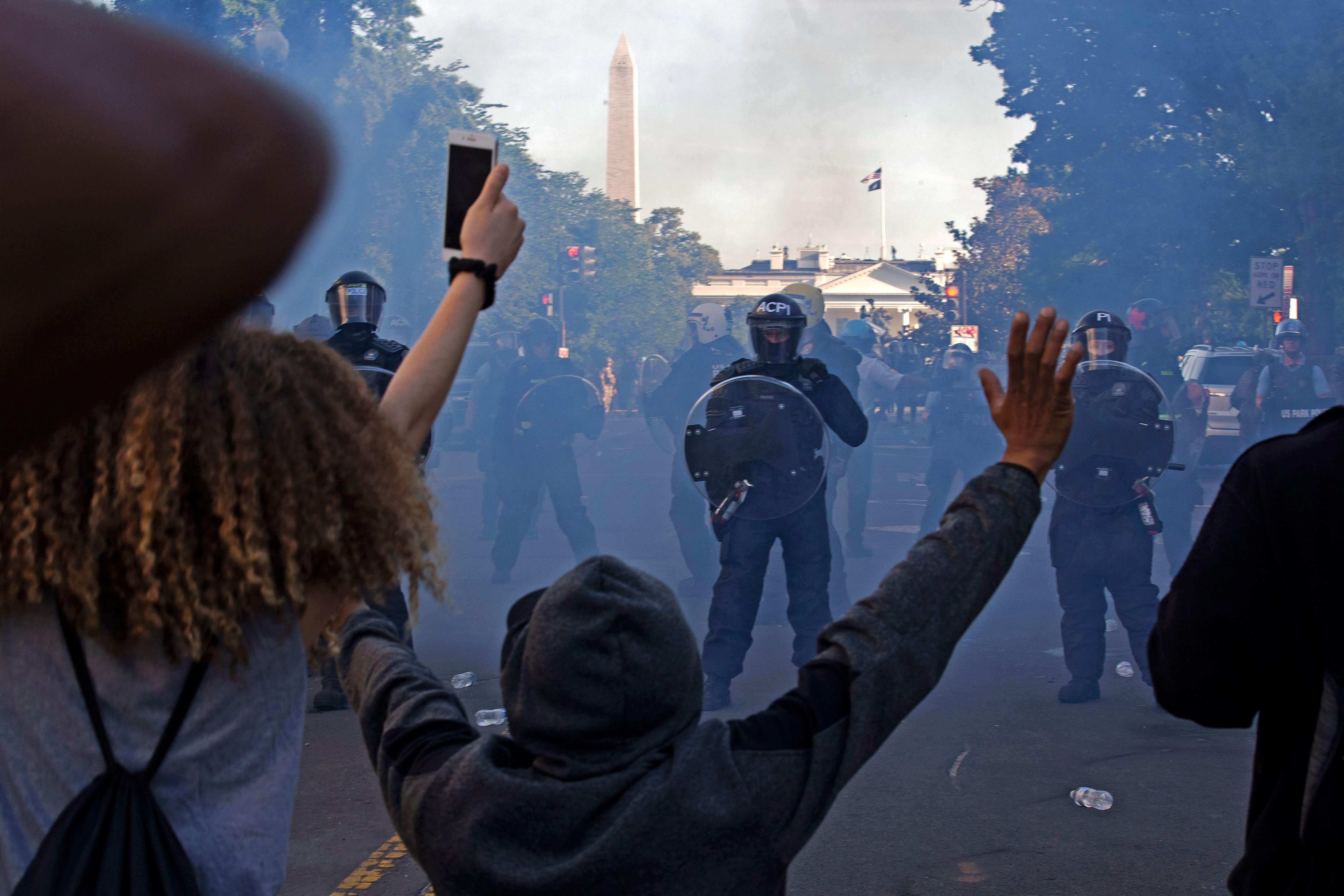 Protesters raise their hands as Secret Service officers can be seen through smoke on a street.