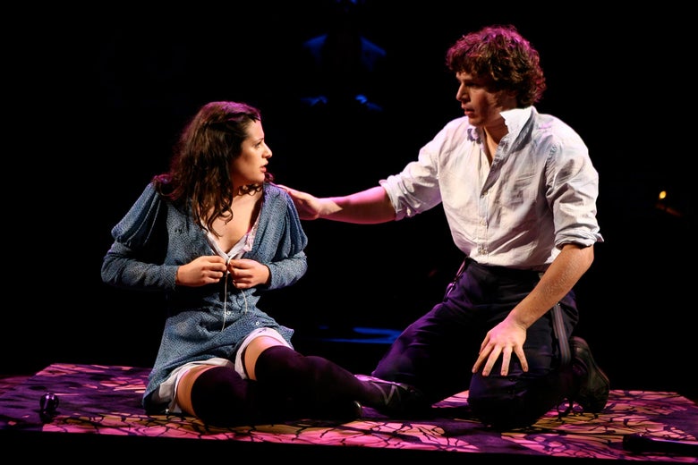 A young woman sits on the floor buttoning her top as a young man next to her puts his hand on her shoulder onstage