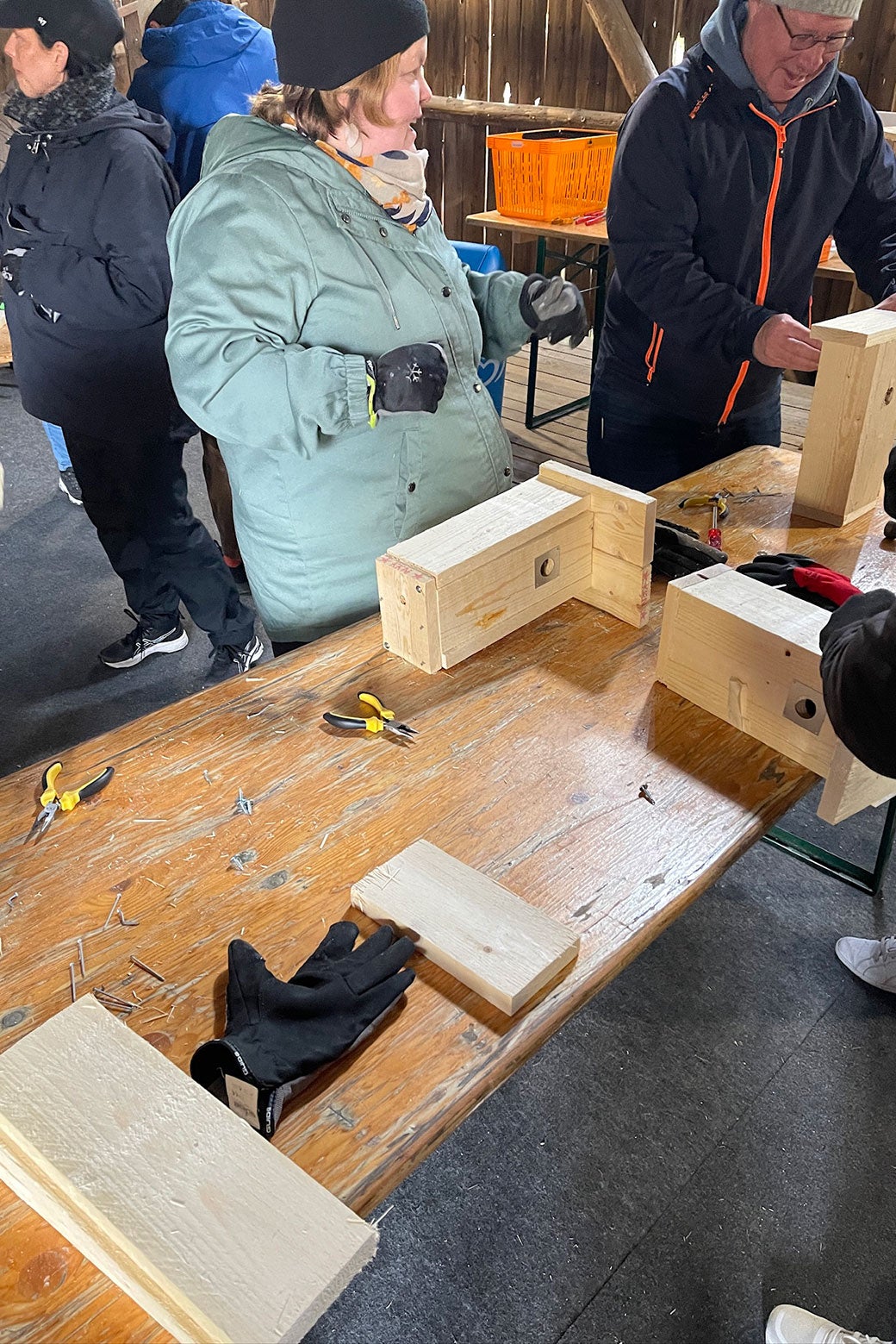People wearing winter coats chat happily over tables outside that they are building birdhouses on.