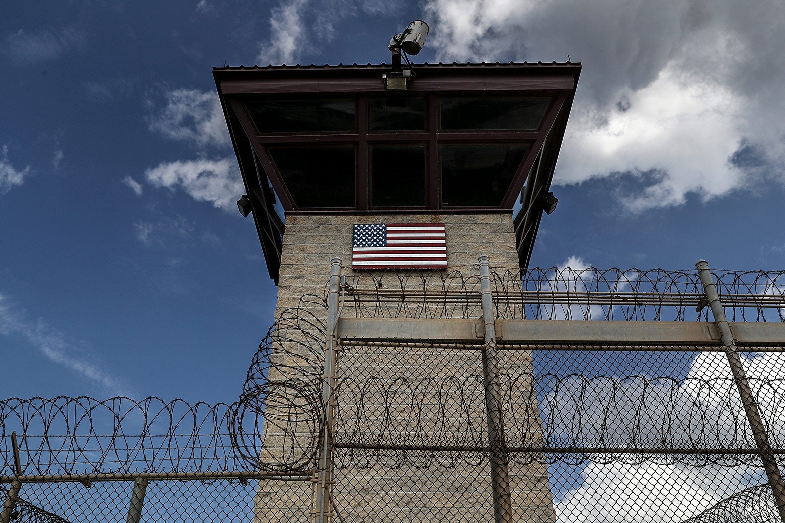 A guard tower marked with an American flag, surrounded by barbed wire
