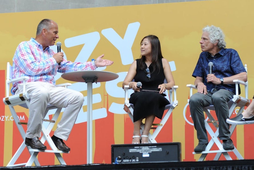 Pinker, sitting in a high folding chair, listens to a moderator's question. There is a woman seated between them onstage and an Ozy Fest backdrop behind them.