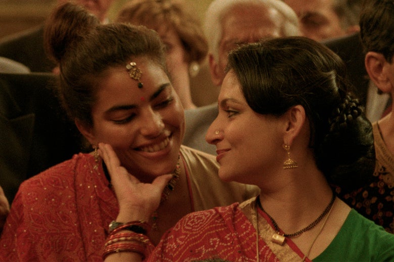 A young woman and a middle-aged woman, both Indian, in traditional wedding garb, look at each other fondly.
