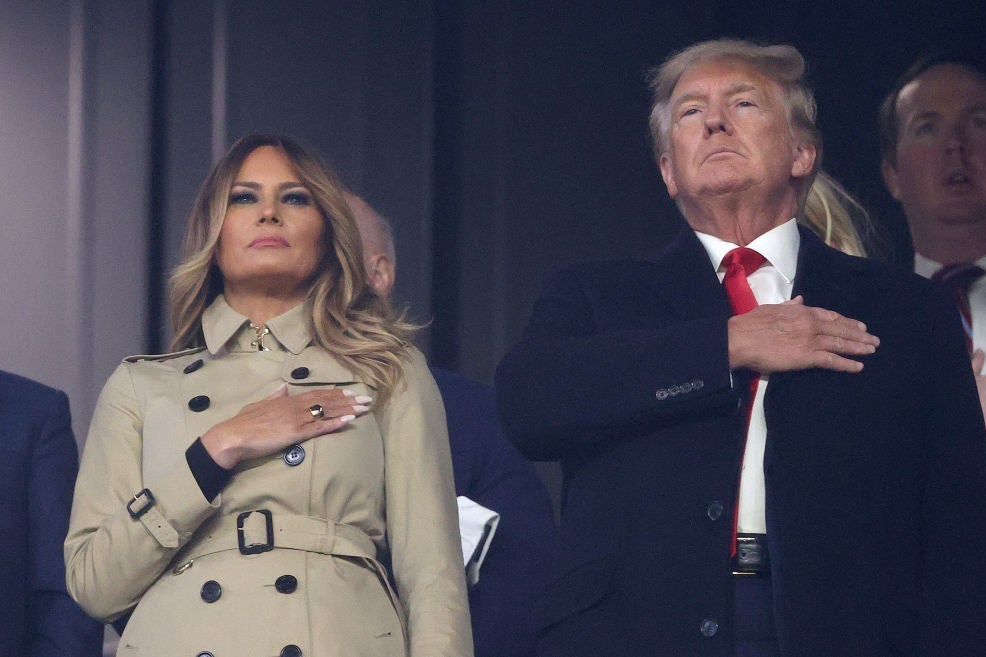 The Trumps, wearing coats, stand with their hands over their hearts.