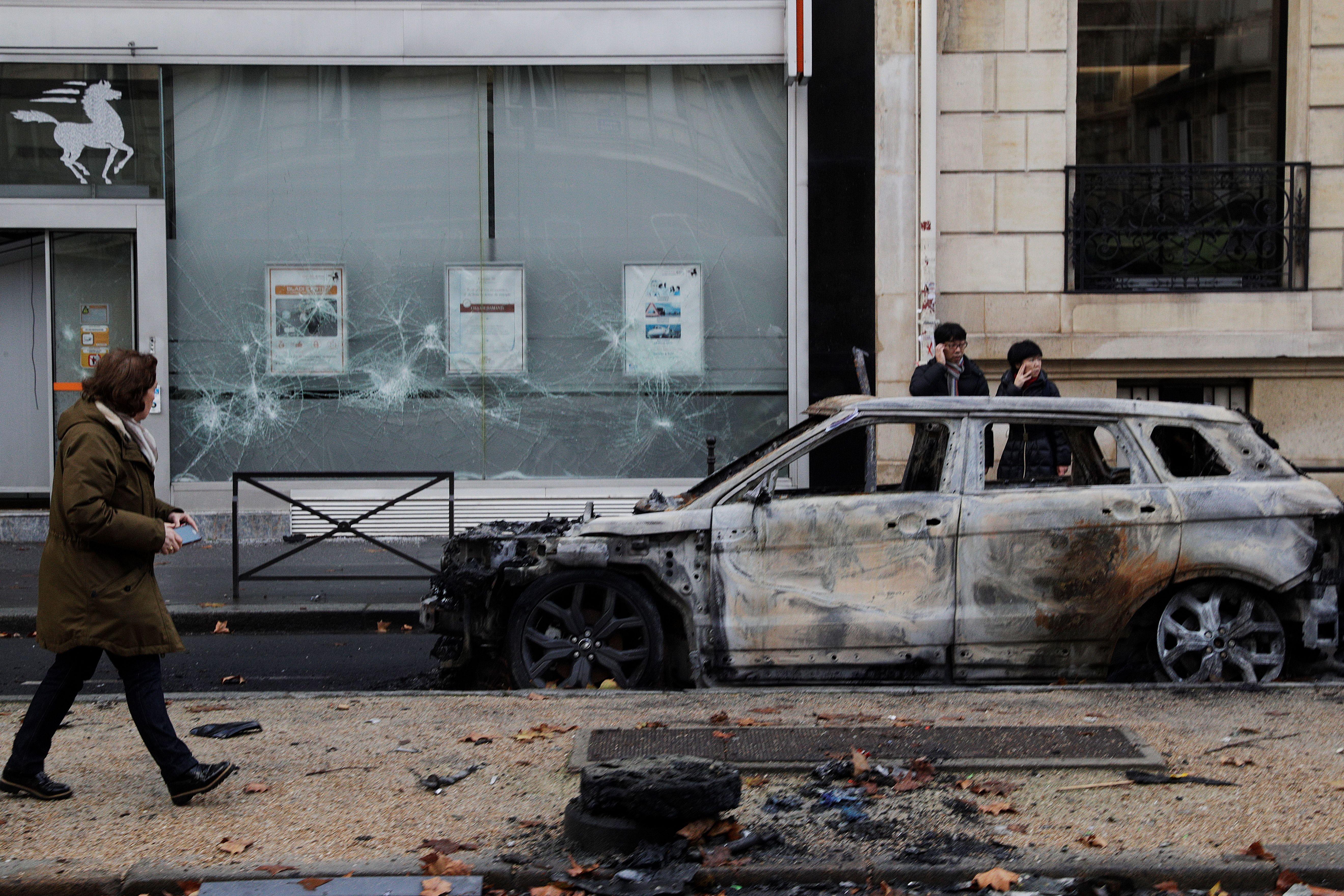 People stand next to a charred car in Paris on December 2, 2018.