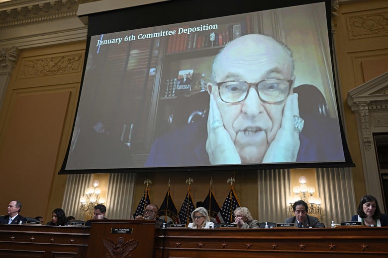 Panel members seated below a screen showing Giuliani clutching his face with both hands in distress