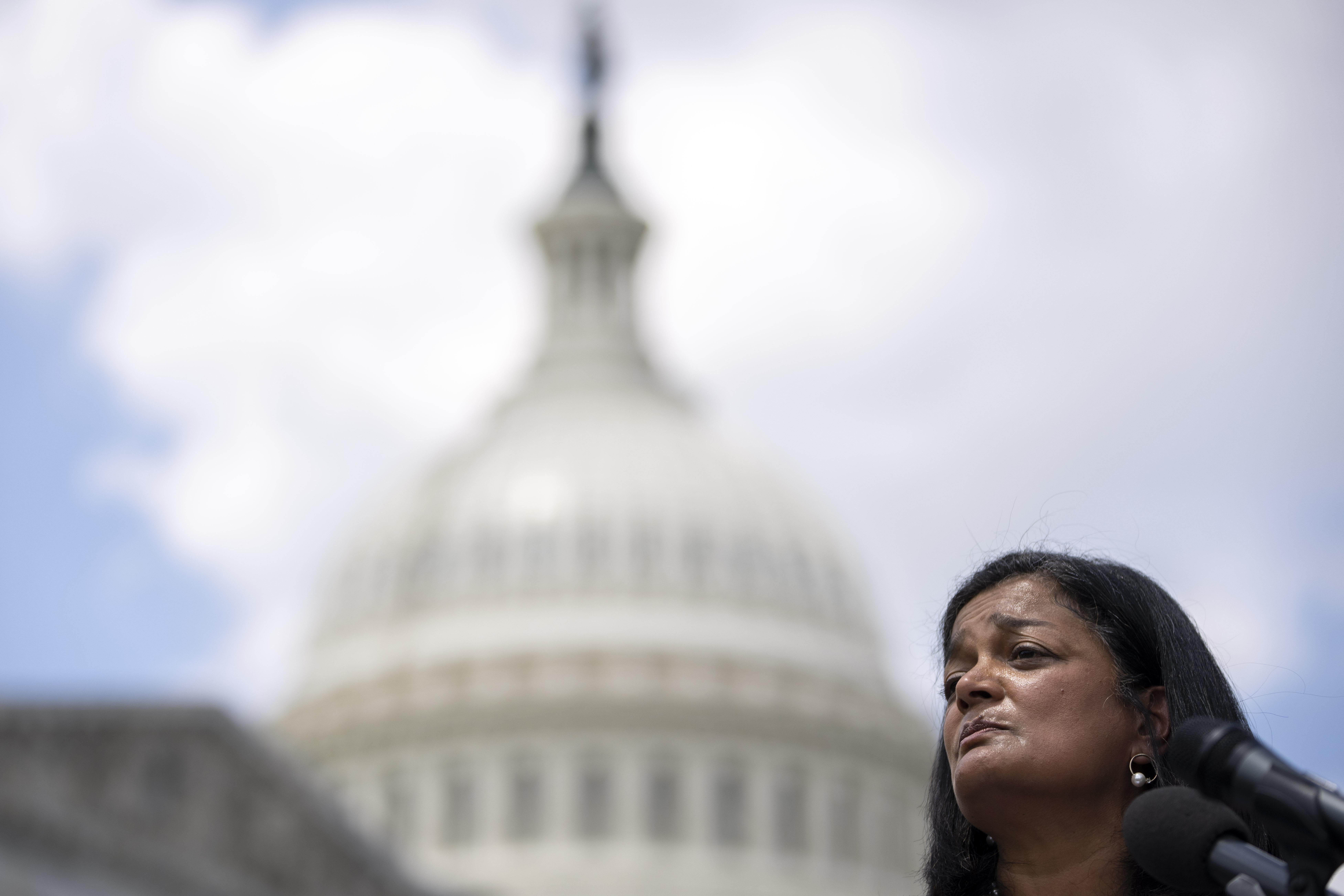 Rep. Pramila Jayapal (D-WA) speaks during a news conference with the Capitol and a cloudy sky behind her.