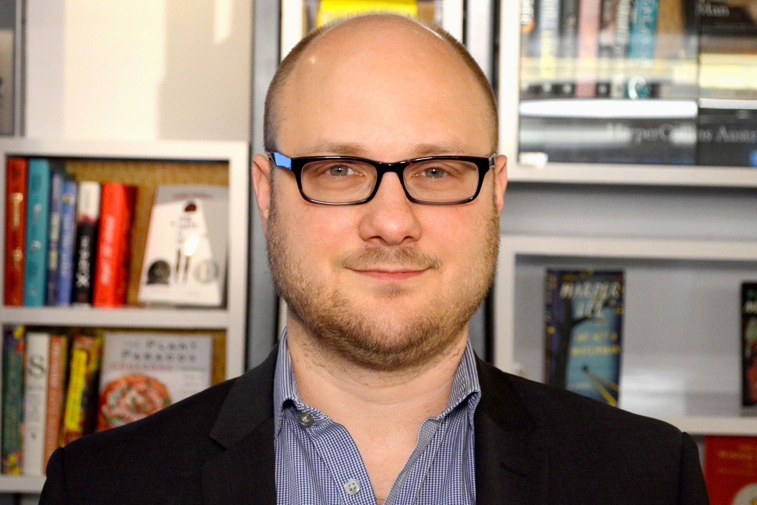 The interviewee stands smiling in front of bookshelves