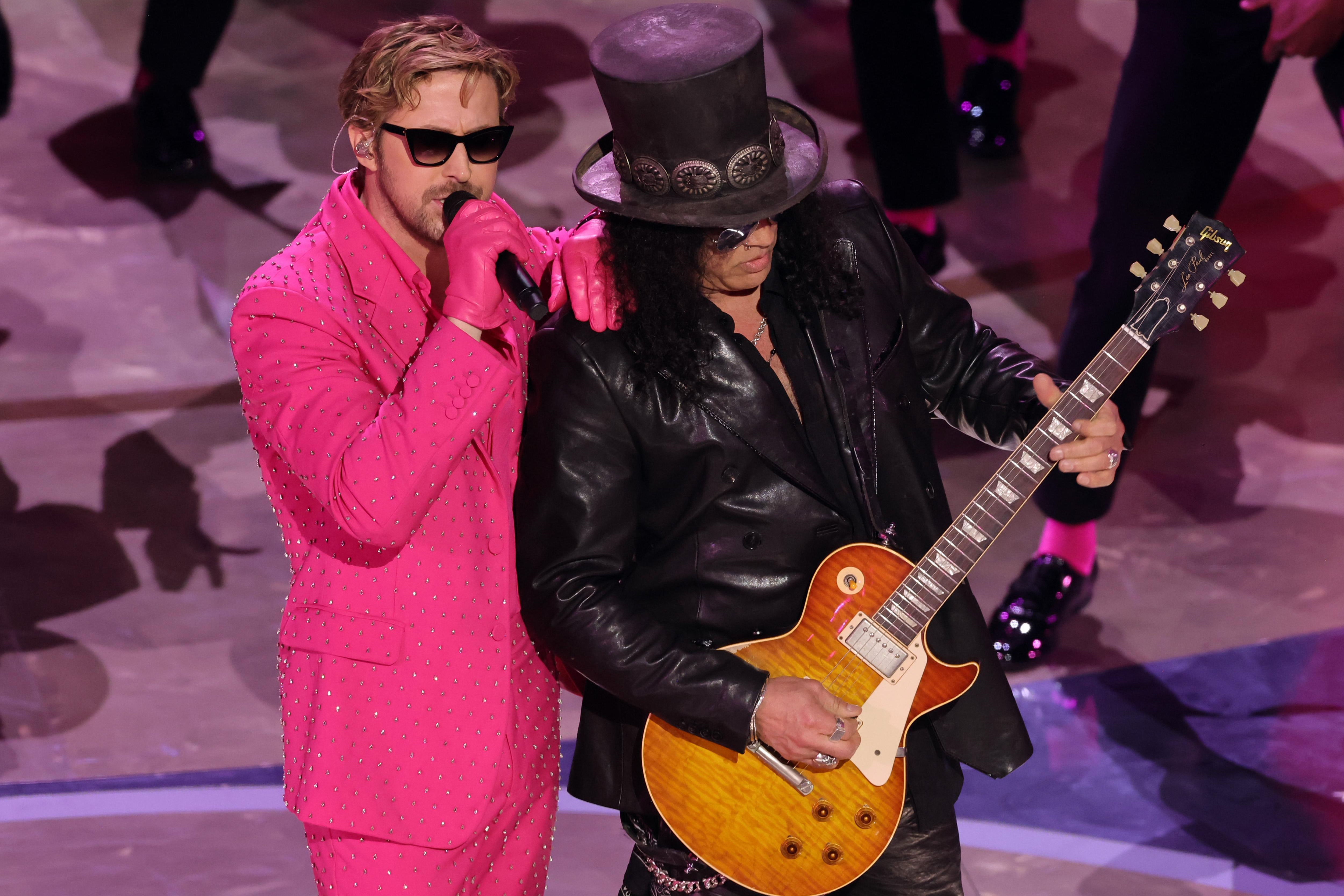 Gosling wears sunglasses, an all-pink suit, and pink gloves. Next to him, Slash wears black leather and his signature top hat, his axe in his hands.