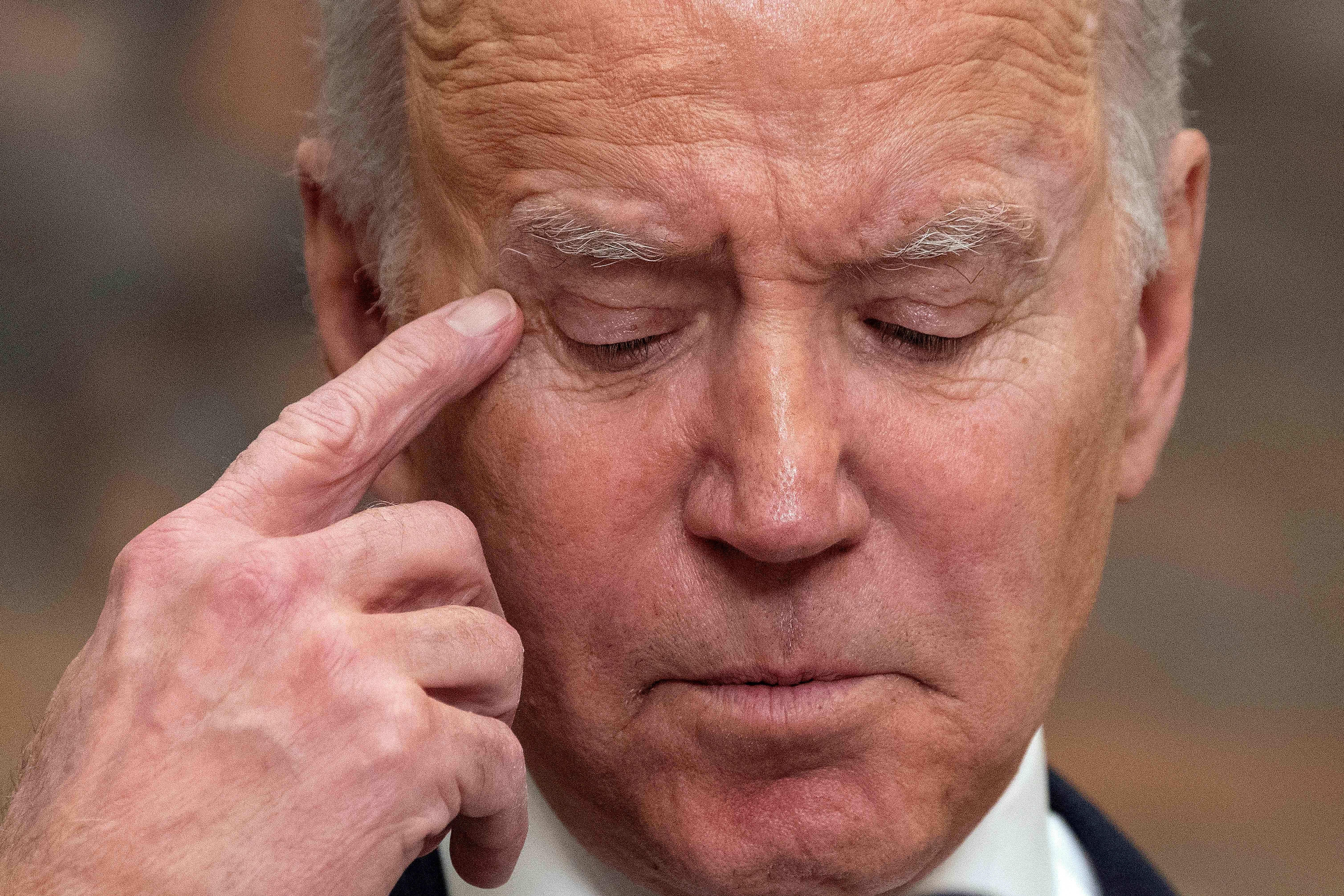 A closeup of Biden's face as he points his right index finger towards his right temple.