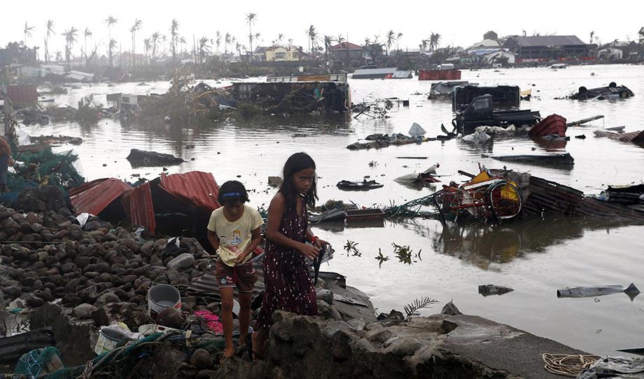 Residents walk near vehicles and debris floating on a river after Super Typhoon Haiyan devastated Tacloban city in central Philippines November 10, 2013. 
