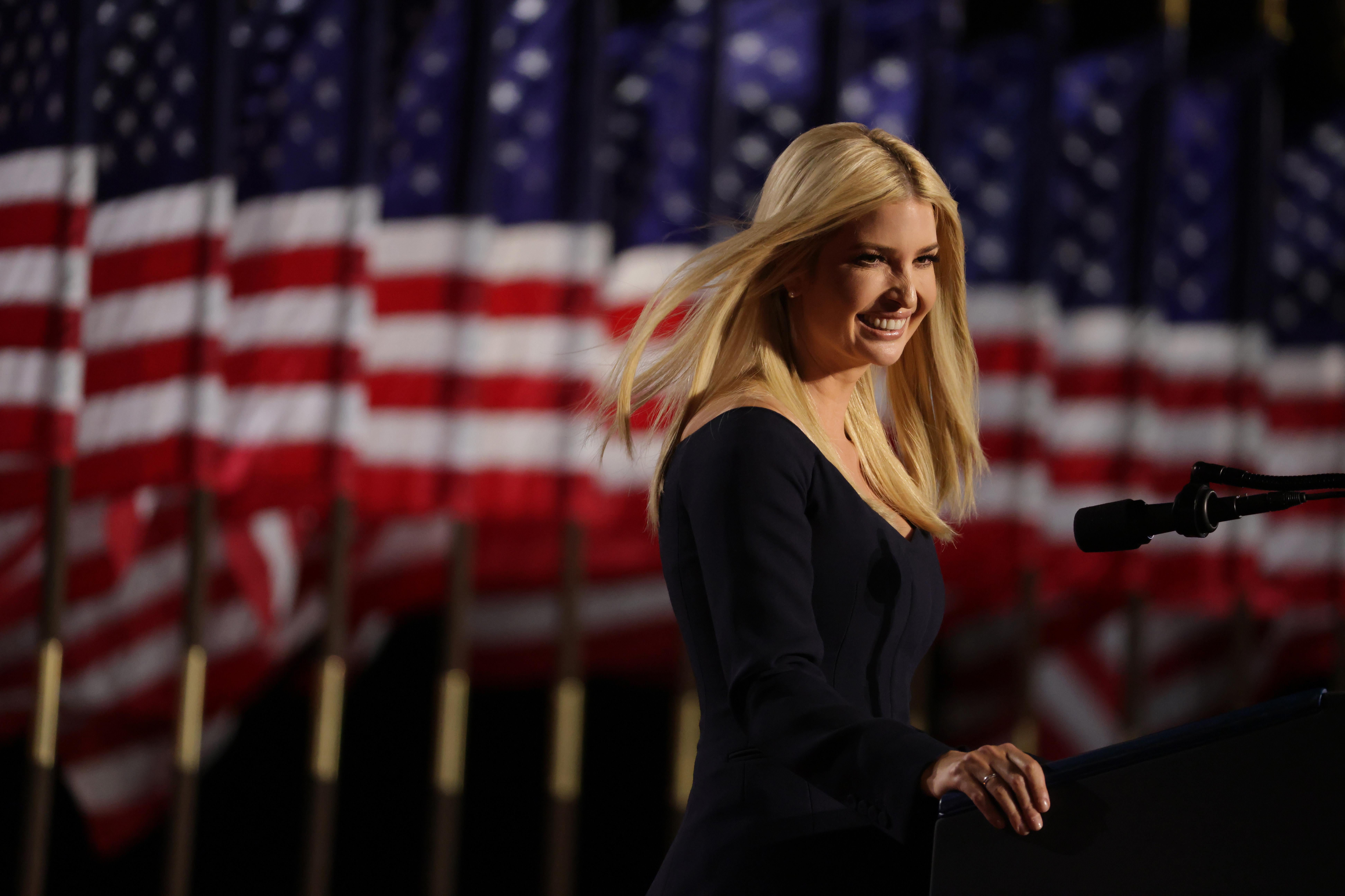 Ivanka Trump standing at a podium, smiling, with American flags in the background
