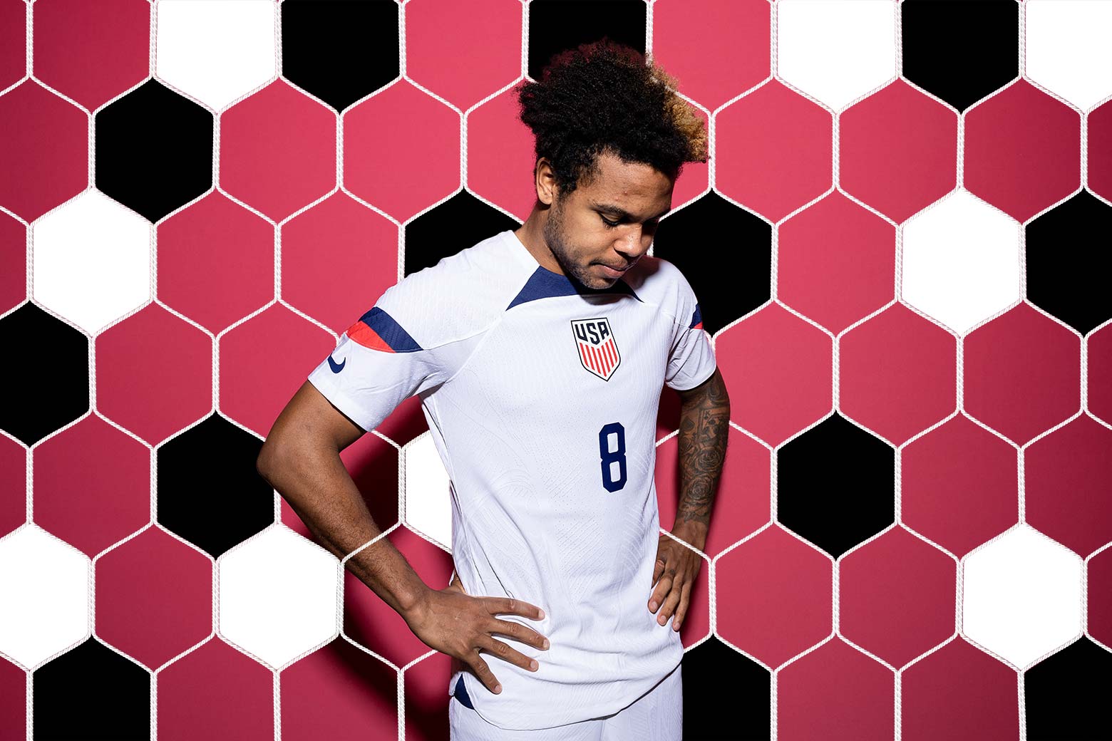 McKennie, arms akimbo, looking down at the ground, the octagonal grid of a soccer net illustrated in a scrim behind him.