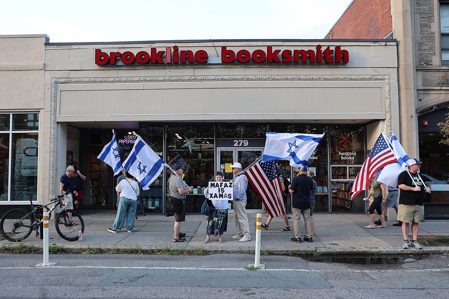 Protesters assemble outside Brookline Booksmith, a book store. One holds a sign accusing the moderator of being part of the group Hamas.