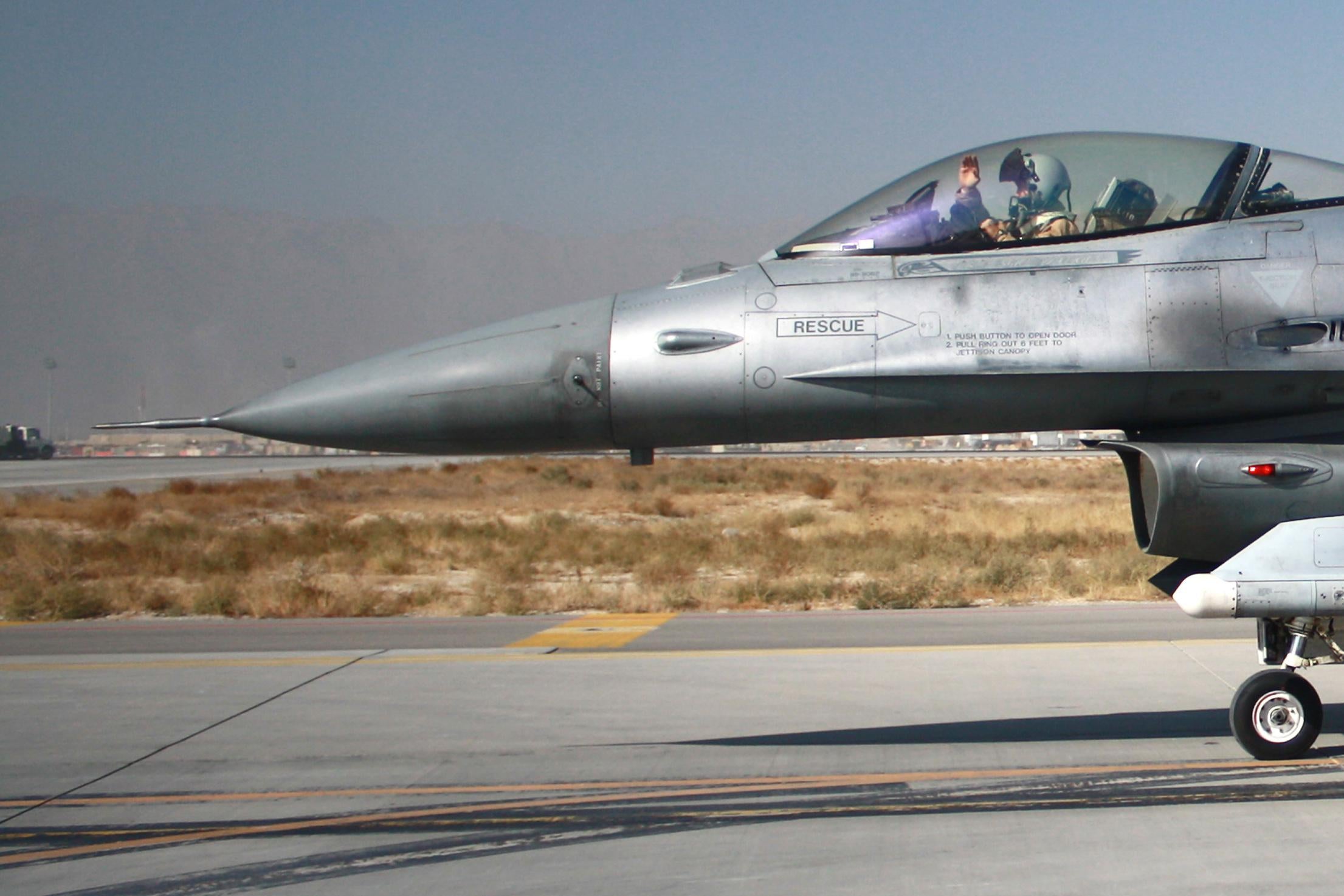 A pilot waves from the cockpit of a fighter jet taxiing on a runway