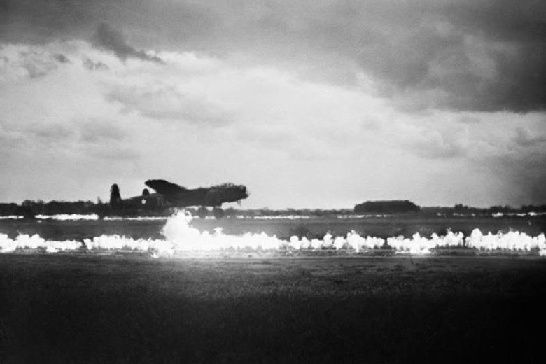 A bomber takes off from a runway flanked by lines of fire under a stormy sky