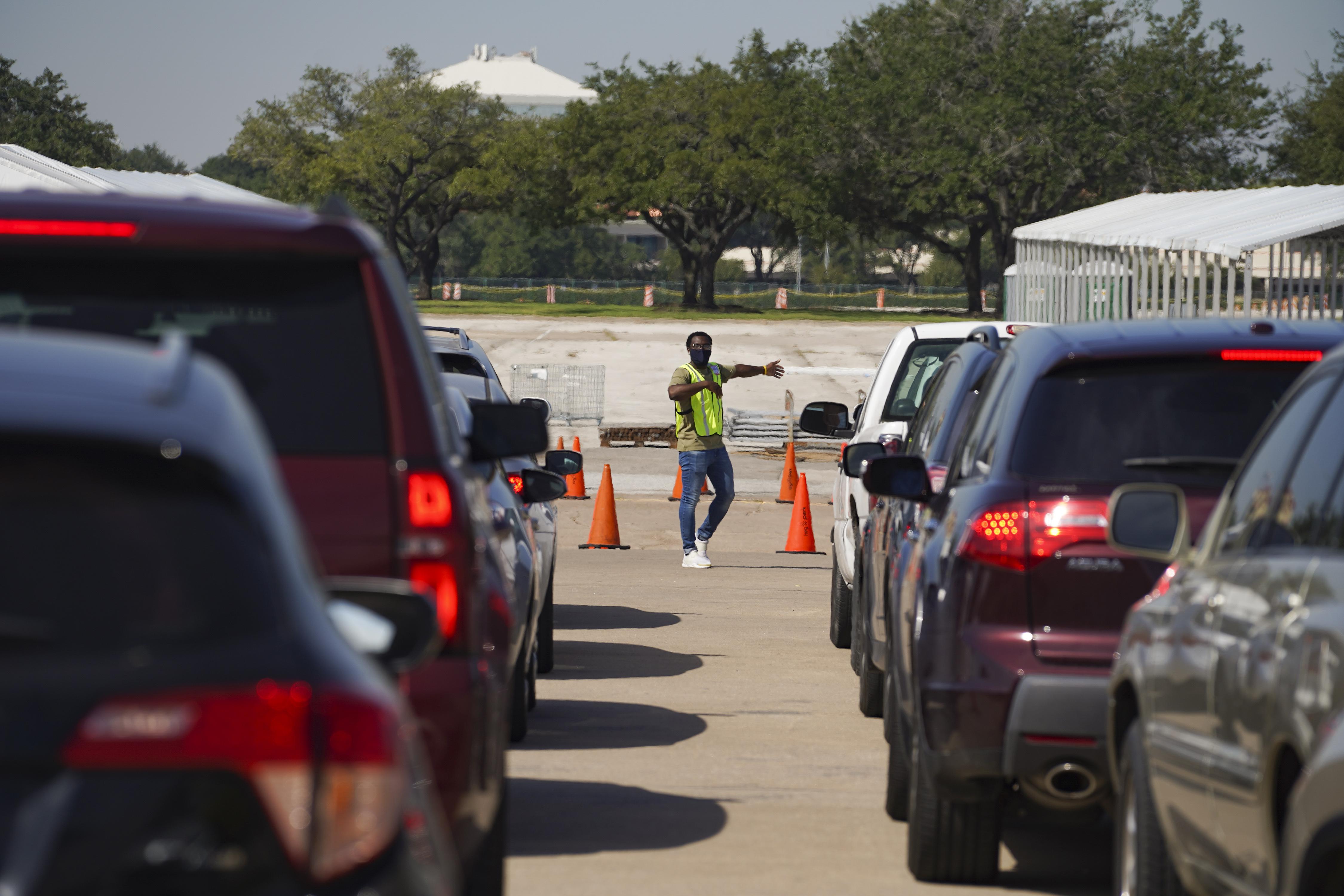 A man in a yellow vest stands between two lanes of cars, directing traffic around the drop-off site.
