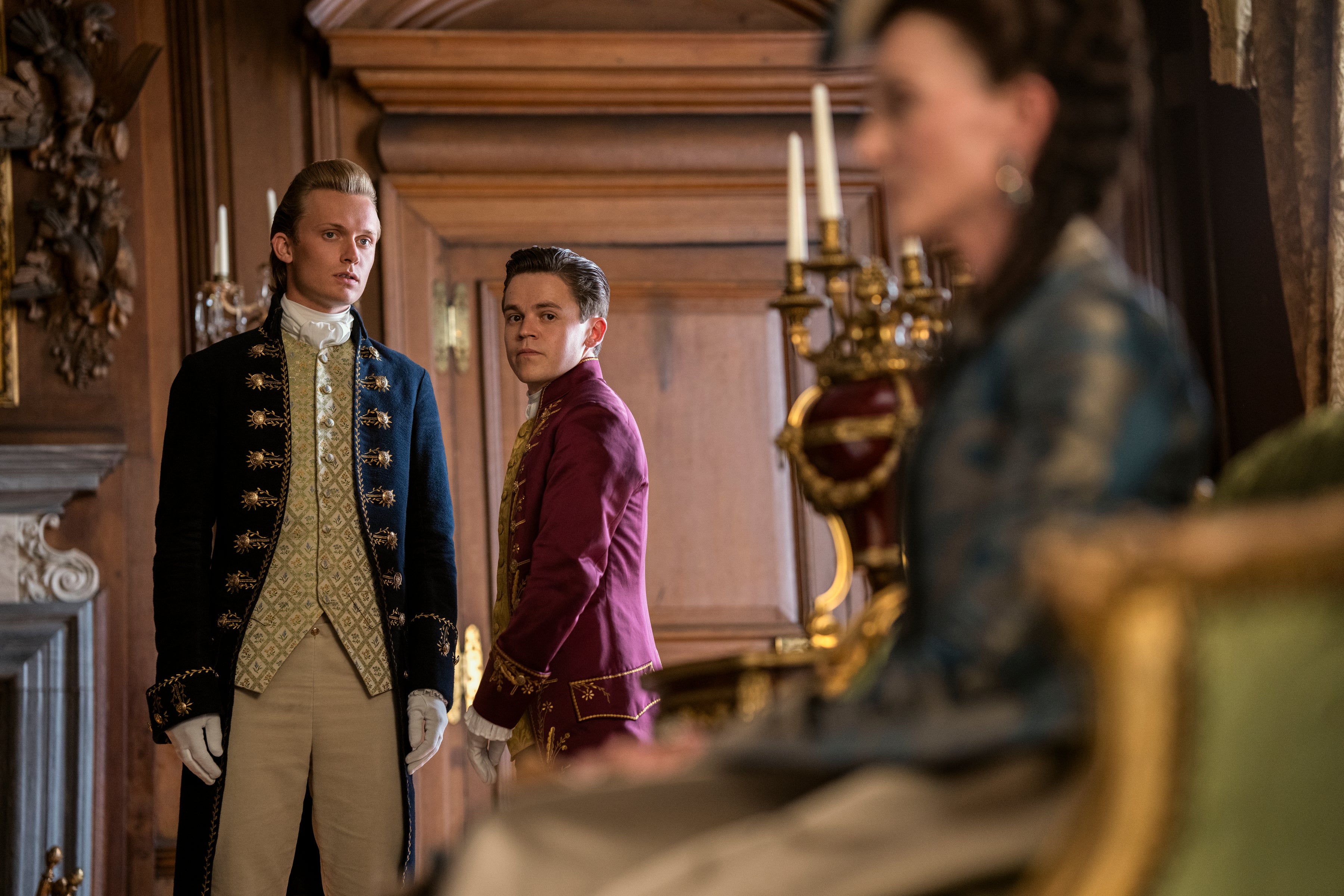 Reynolds and Brimsley converse in a lavish hallway.