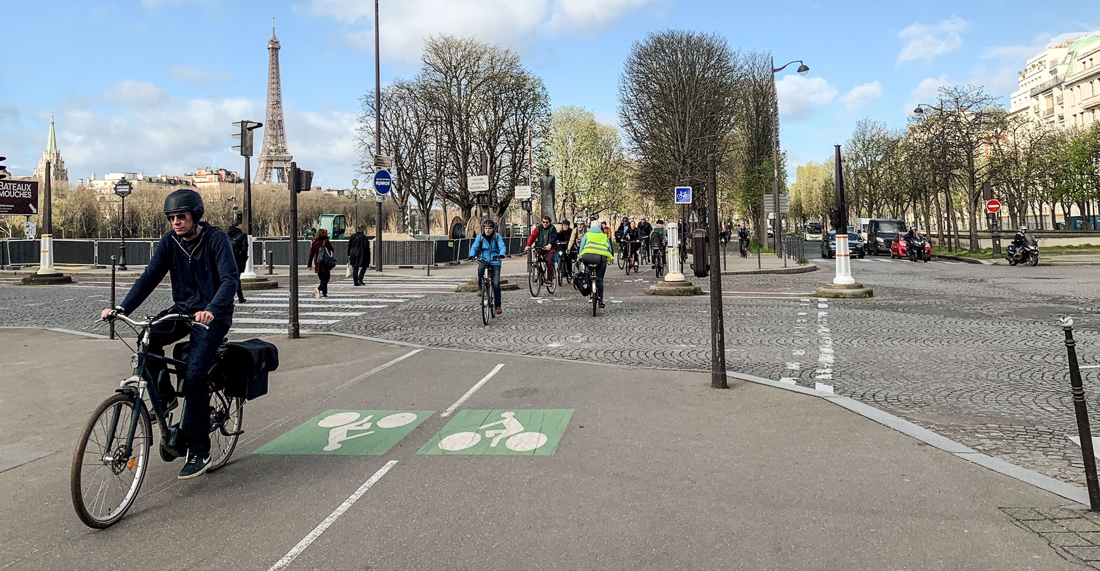 A man wearing a helmet rides his bike down a cobblestone Paris street near the Eiffel Tower.