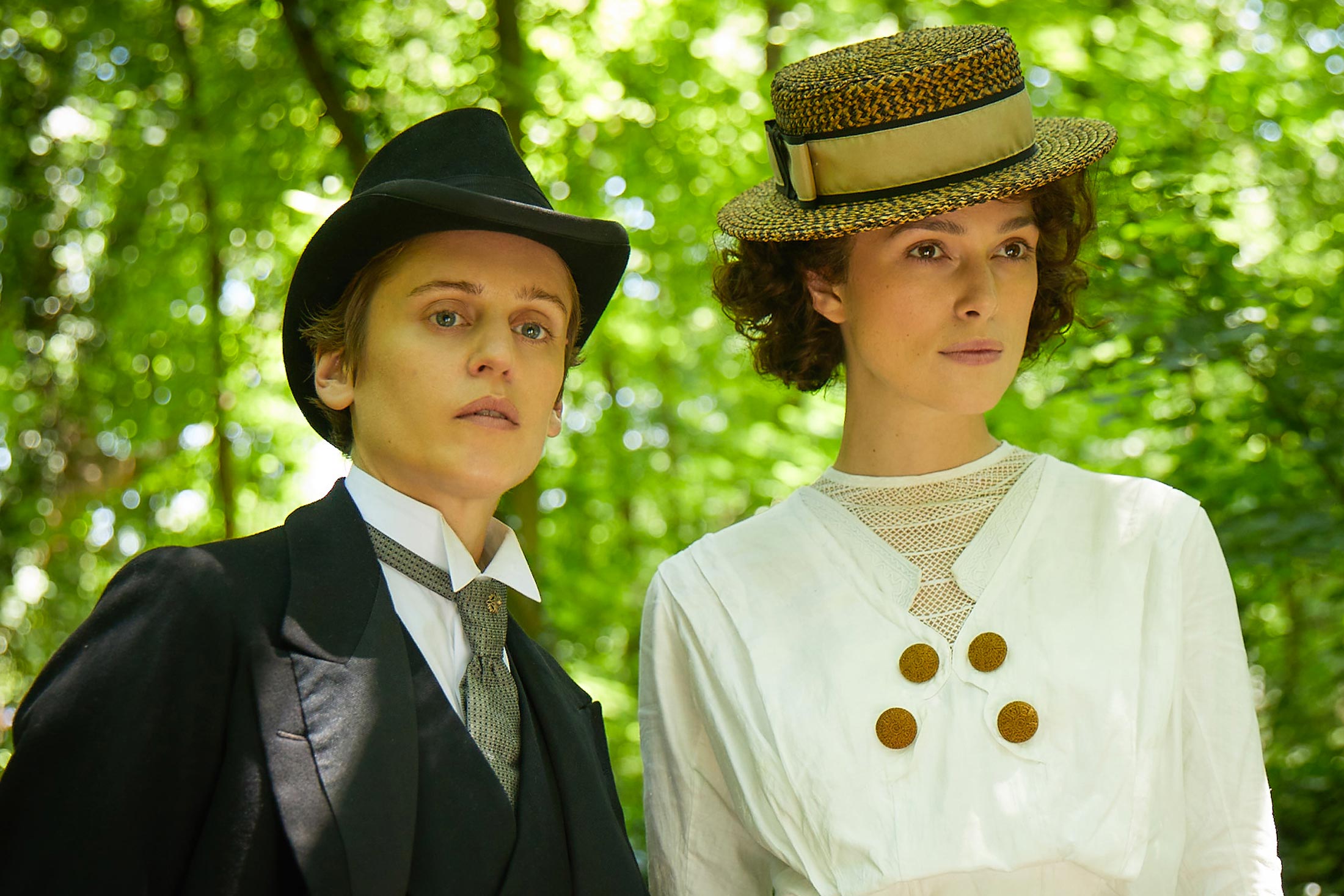 Denise Gough in a masculine suit and Keira Knightley in a white dress and straw hat.