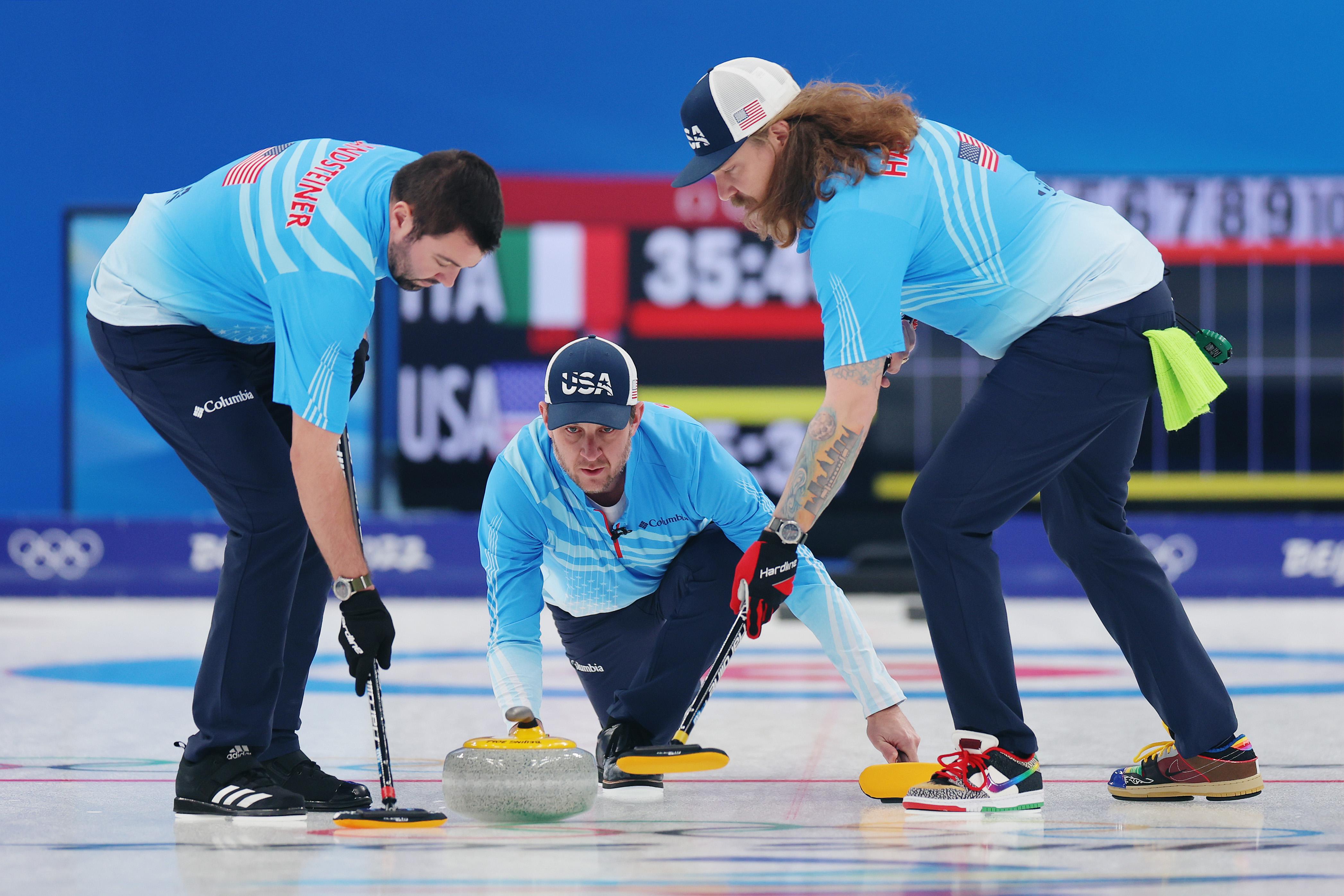A curler prepares to throw a rock while two teammates stand beside him.