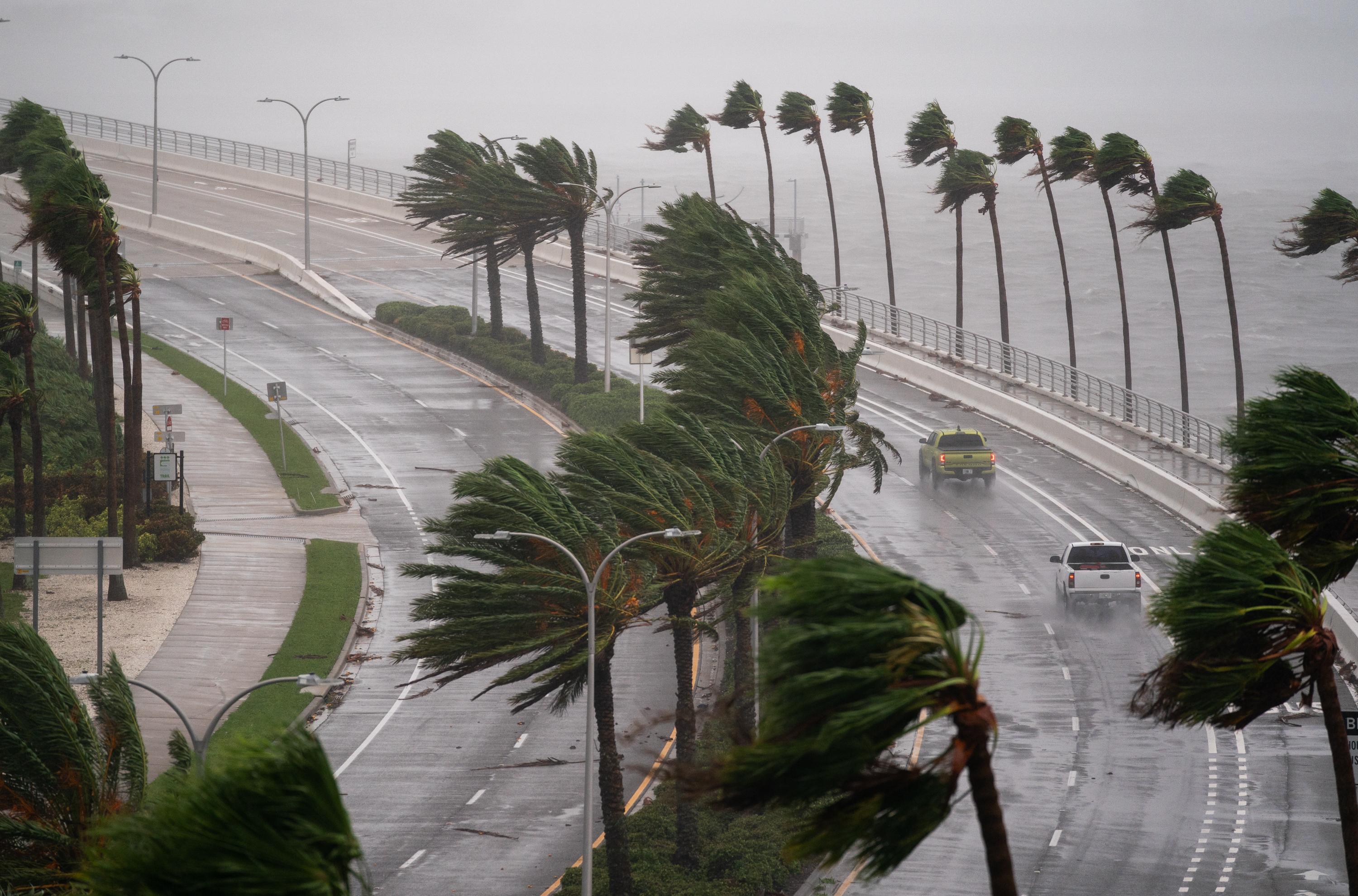 Motorists travel across the John Ringling Causeway as Hurricane Ian churns to the south on Sept. 28 in Sarasota, Florida. The palm trees are being blown across the street.