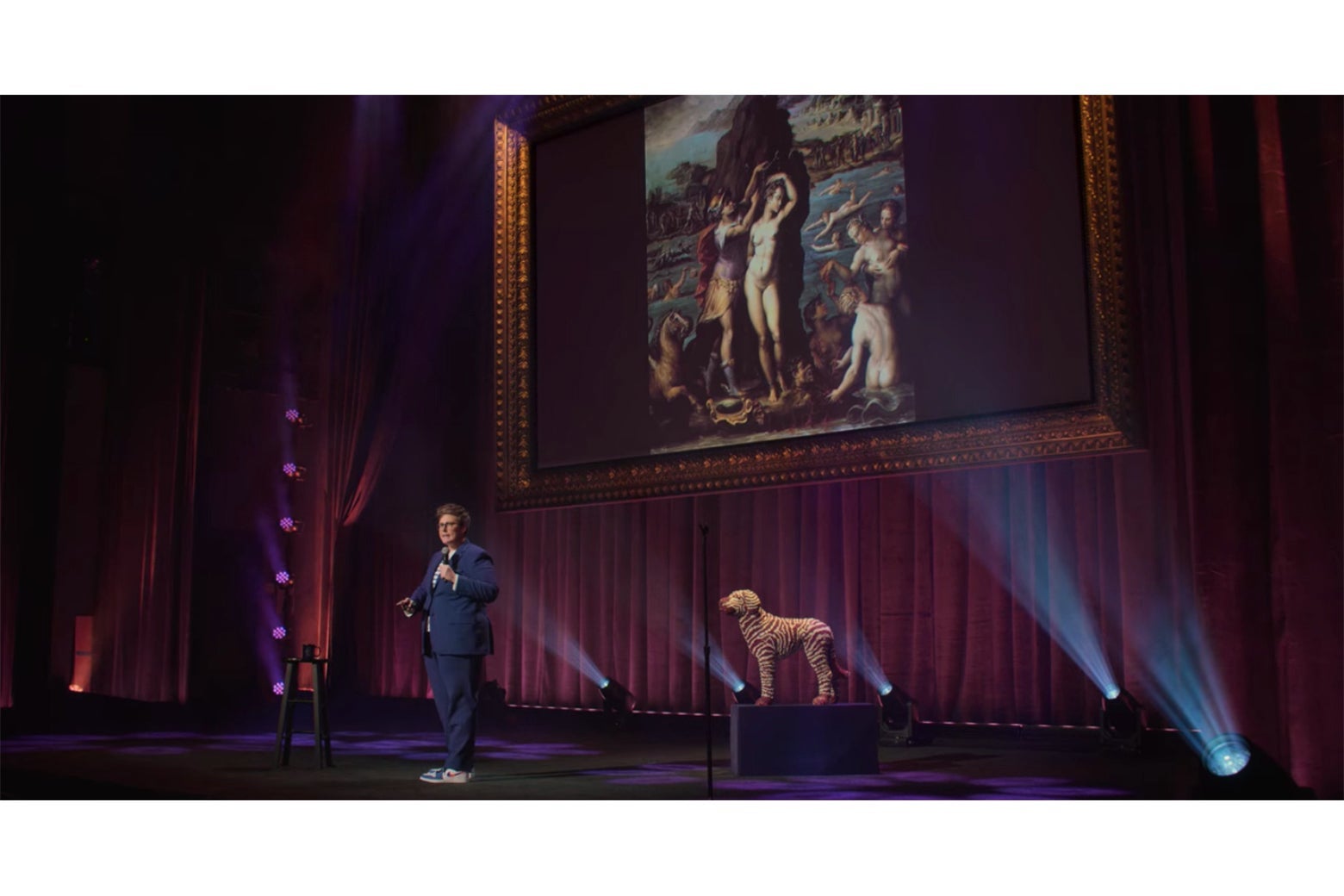 Hannah Gadsby stands in front of a projection of Vasari's Perseus and Andromeda.
