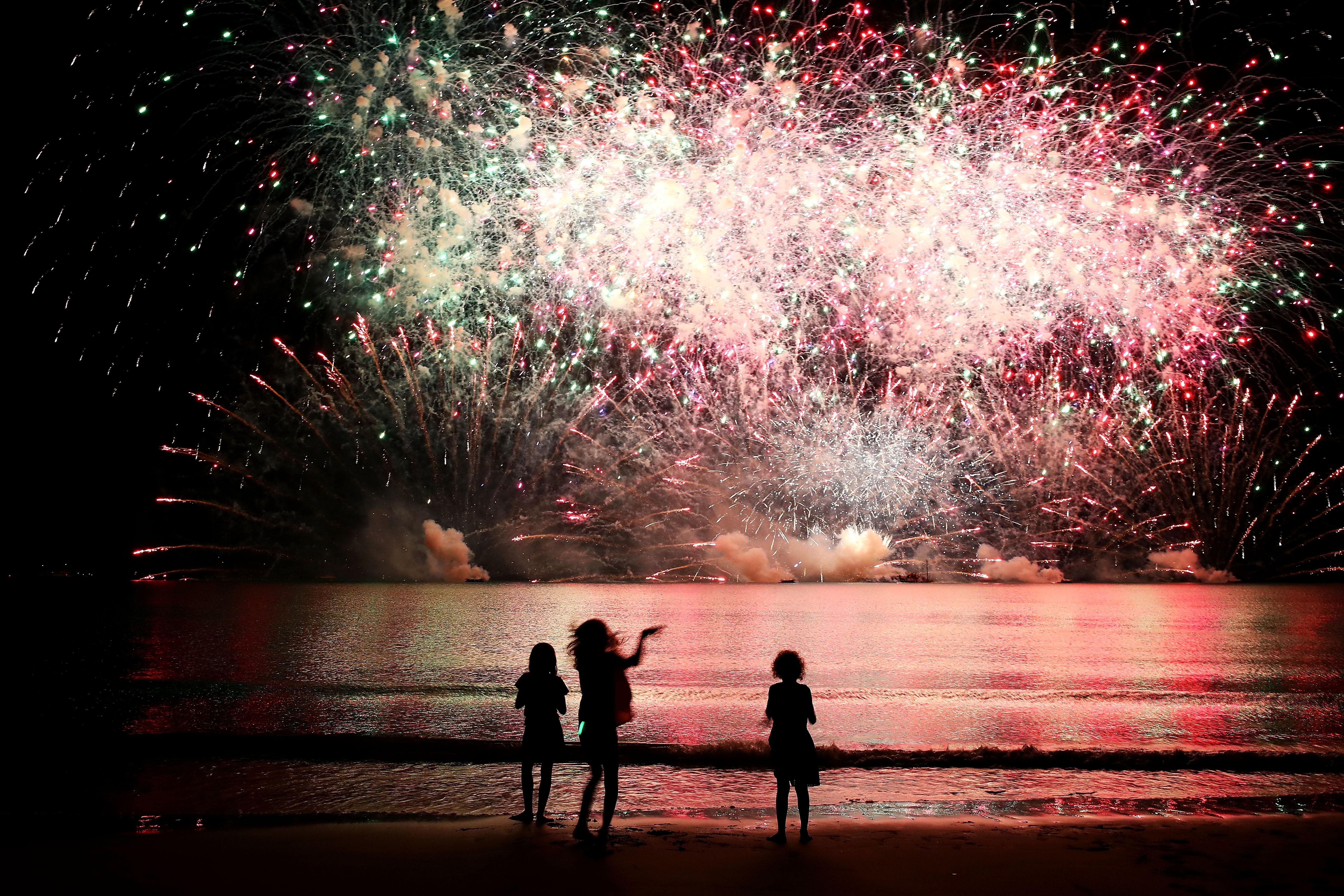 Young girls watch a fireworks display on a beach.