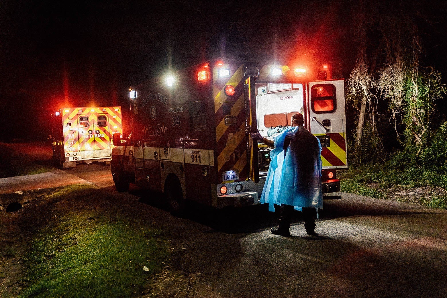A person in PPE opens the back doors to an ambulance in the dark.