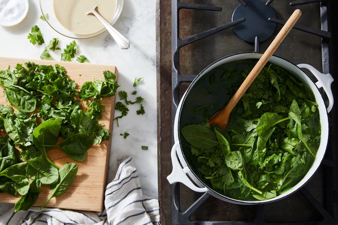 A bowl of green herbs next to a cutting board.