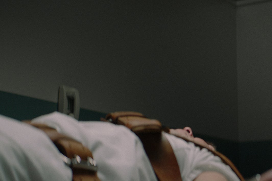 Alfre Woodard in a blue suit stands over a prone, bound man.