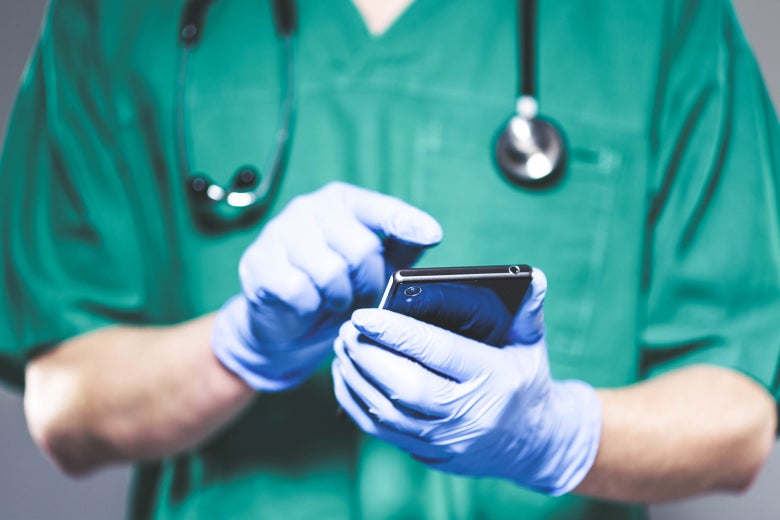  A doctor in scrubs, wearing gloves, looking at a cellphone.