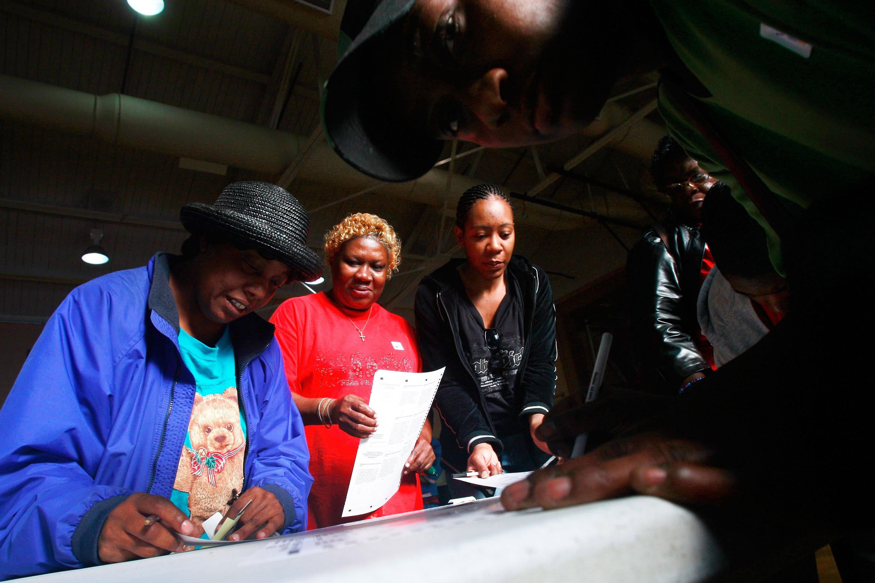 Black women stand in a line filling out ballots
