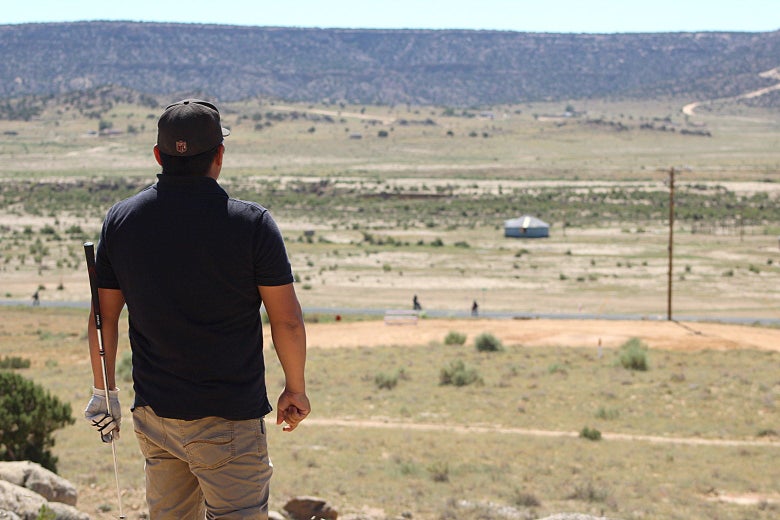 A man holding a golf club looks out over a desert vista.