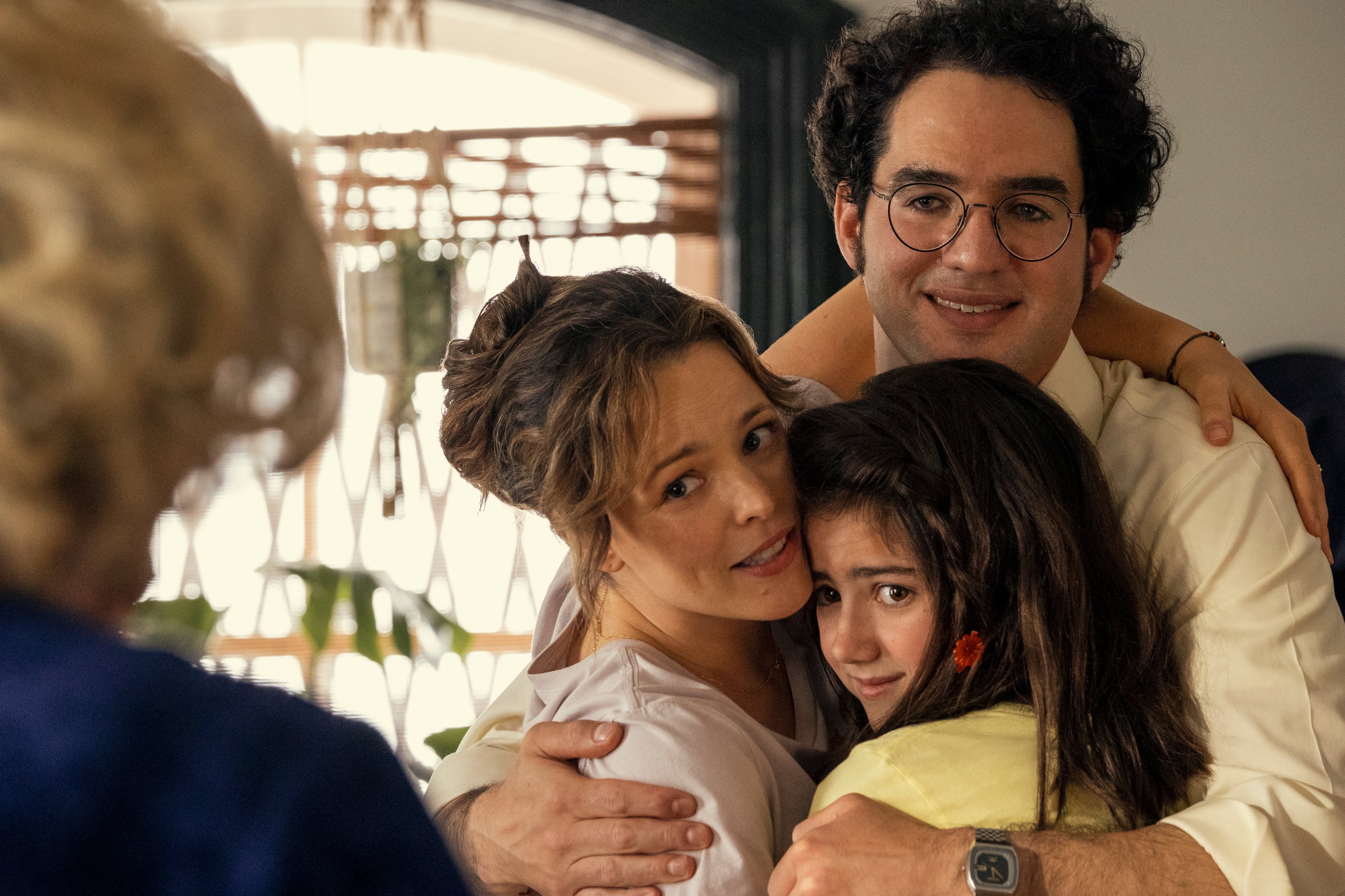 The three stand in a group hug, looking very ’70s, while staring at a gray-haired woman who's mostly off-screen. The parents smile, while the daughter looks perhaps a little suffocated.