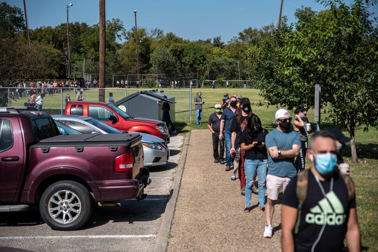 People in face masks line up beside a parking lot.