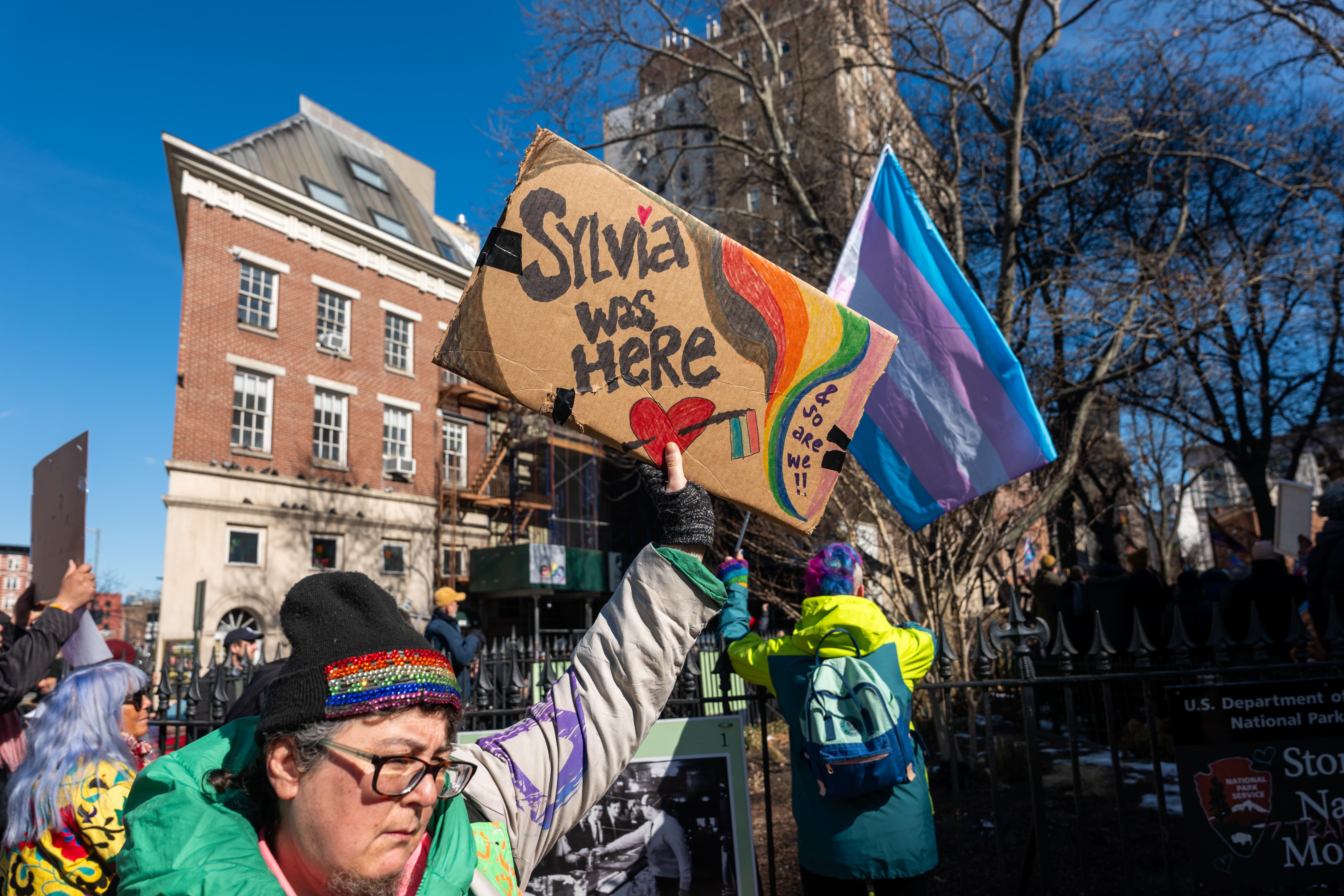 A person holds a protest sign saying "Sylvia was here" outside of the Stonewall National Monument.