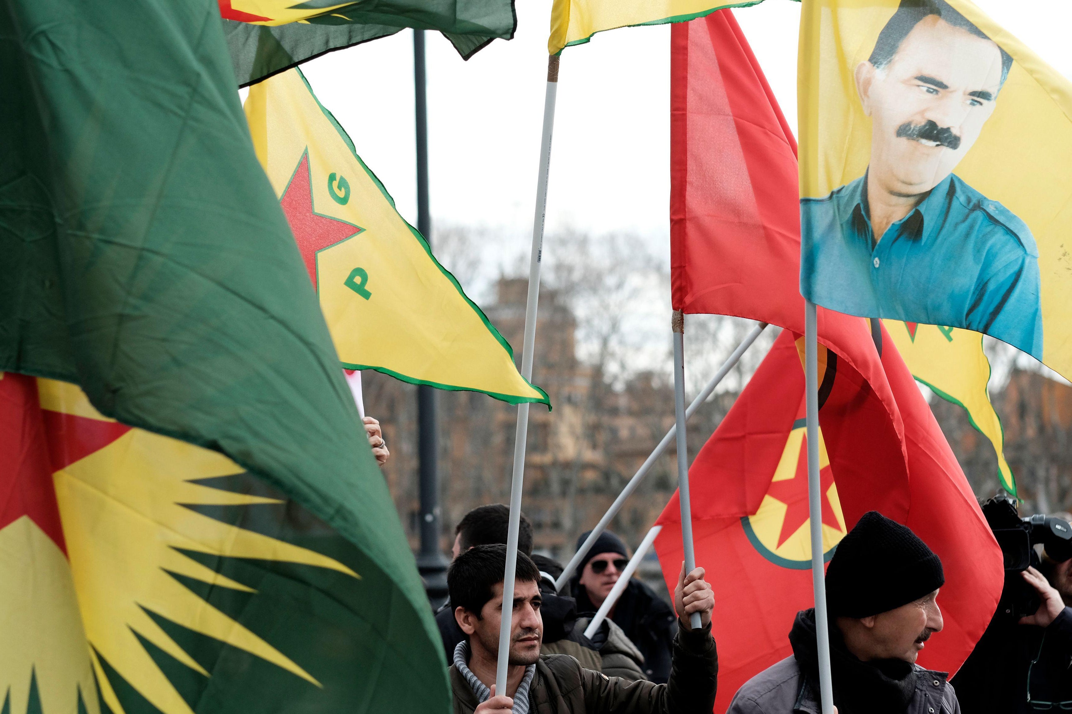 Demonstrators wave red and yellow Kurdish flags alongside a portrait of Abdullah Öcalan.