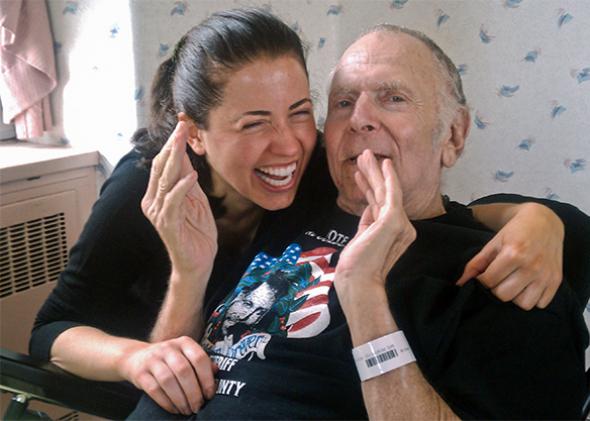 Author Lili Anolik and Al Goldstein at his nursing home last year. Lili laughs as Al holds out his hands to give a rough estimate of his penis size.