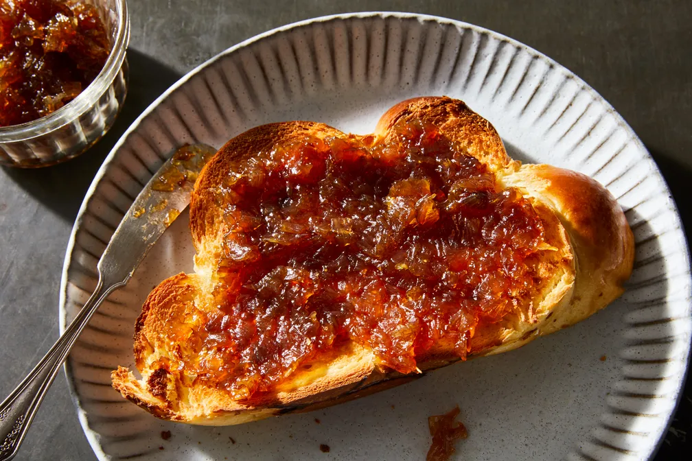 Toast topped with shallot jam next to a butter knife on a plate, with a small glass jar of more shallot jam next to the plate