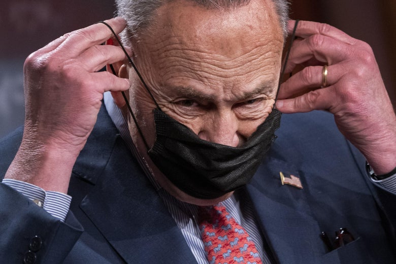 Chuck Schumer tucks the straps of a black surgical mask behind his ears.