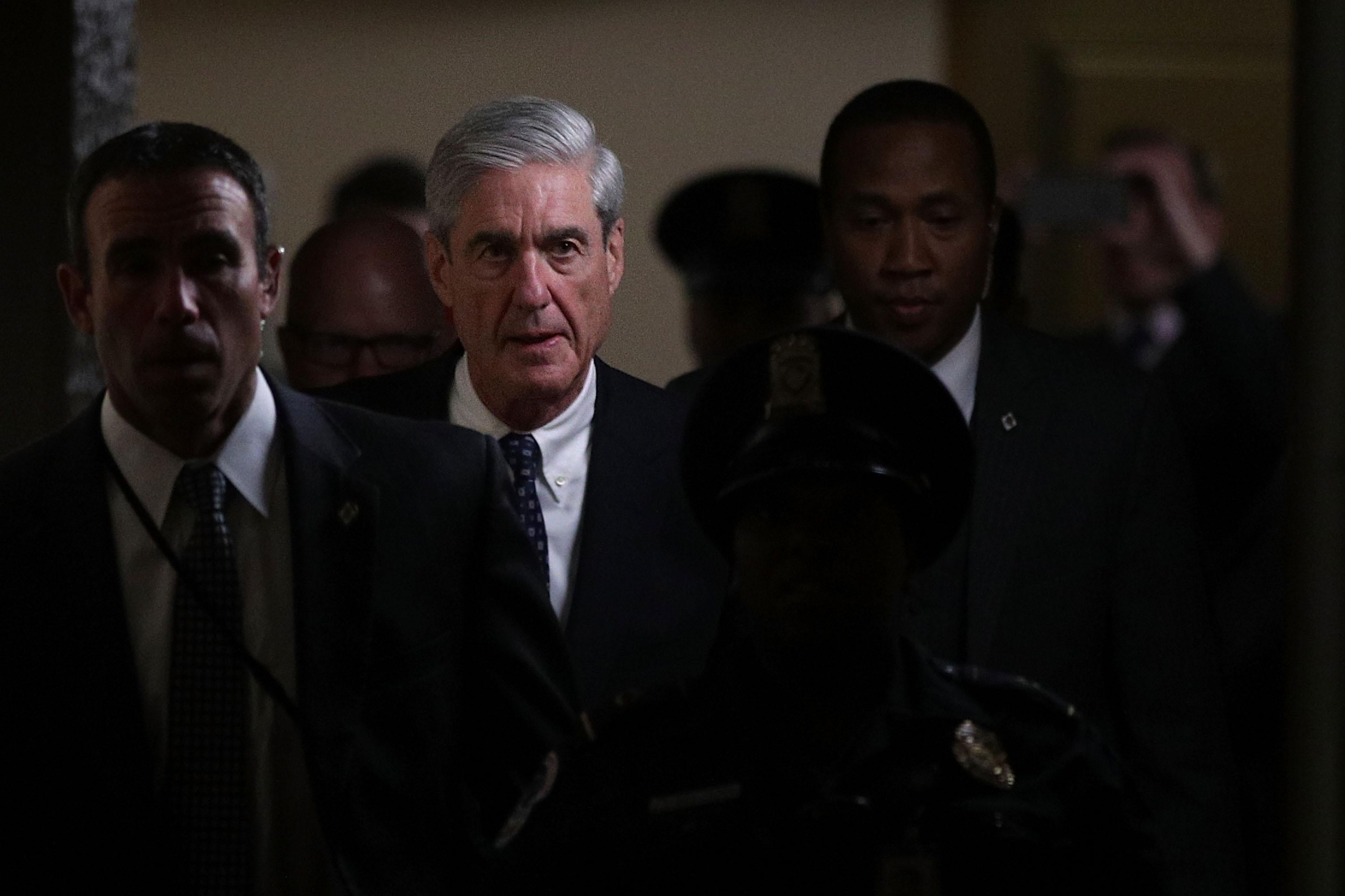 Special counsel Robert Mueller walks down a hallway, surrounded by staffers.