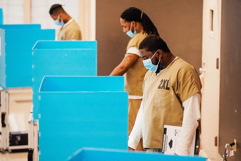Men in brown prison garb standing at blue cardboard booths to vote.