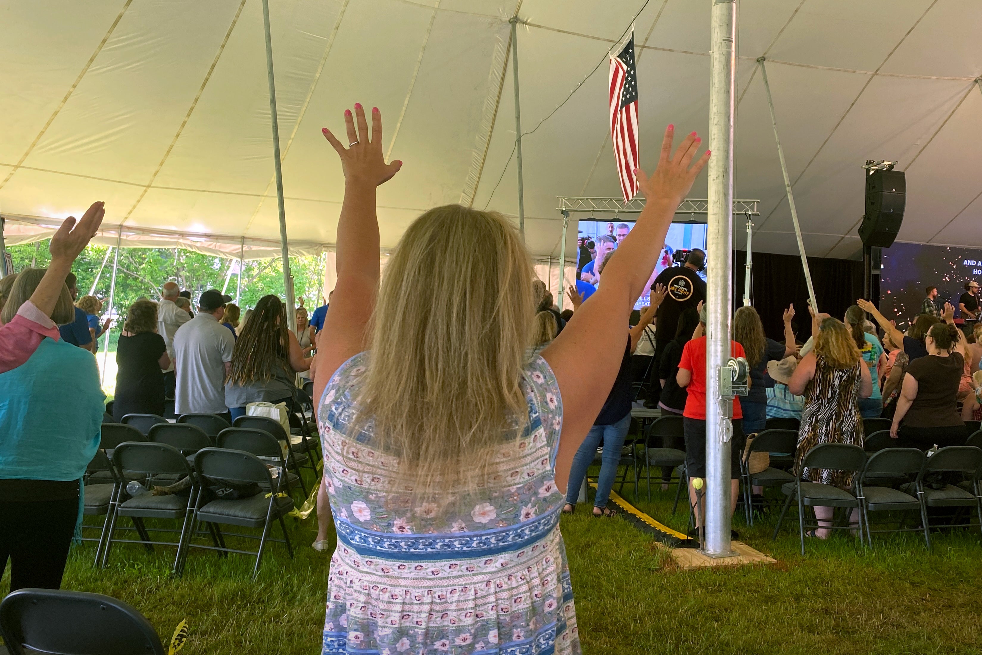 A crowd assembled in a tent raise their hands in prayer.