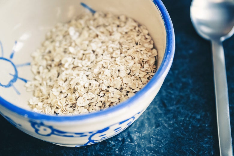 A bowl of uncooked oats beside a metal spoon.