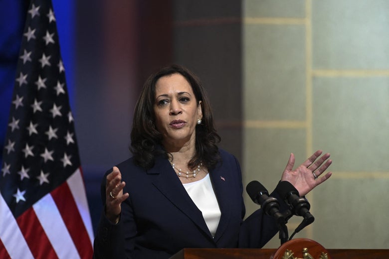 Harris gestures with both hands while speaking at a podium with an American flag behind her