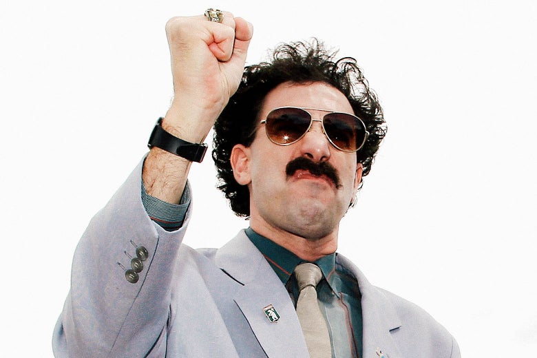 Sacha Baron Cohen, as Borat, raises his fist and scrunches up his face.